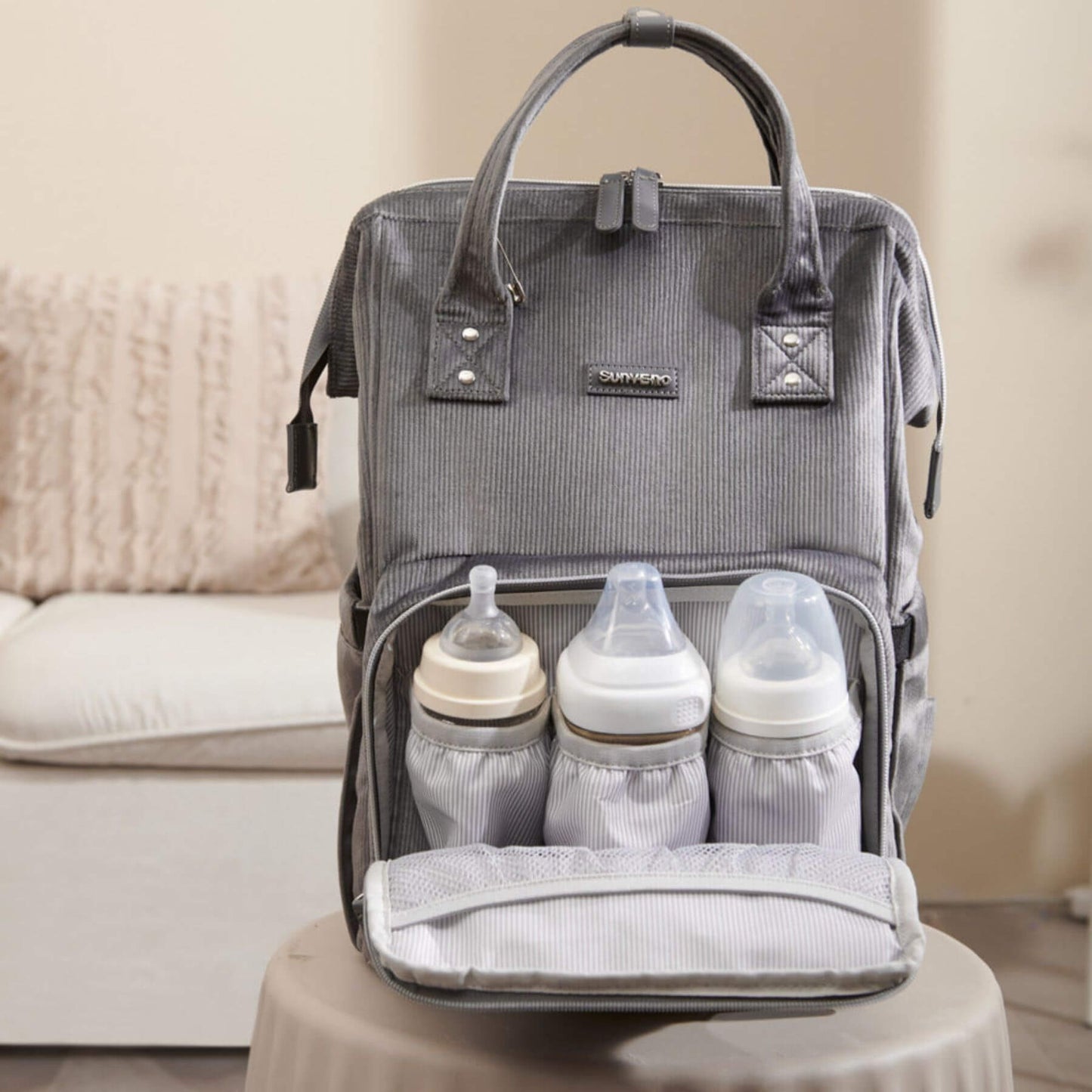 Corduroy Diaper Backpack Grey with baby bottles inside on a beige surface