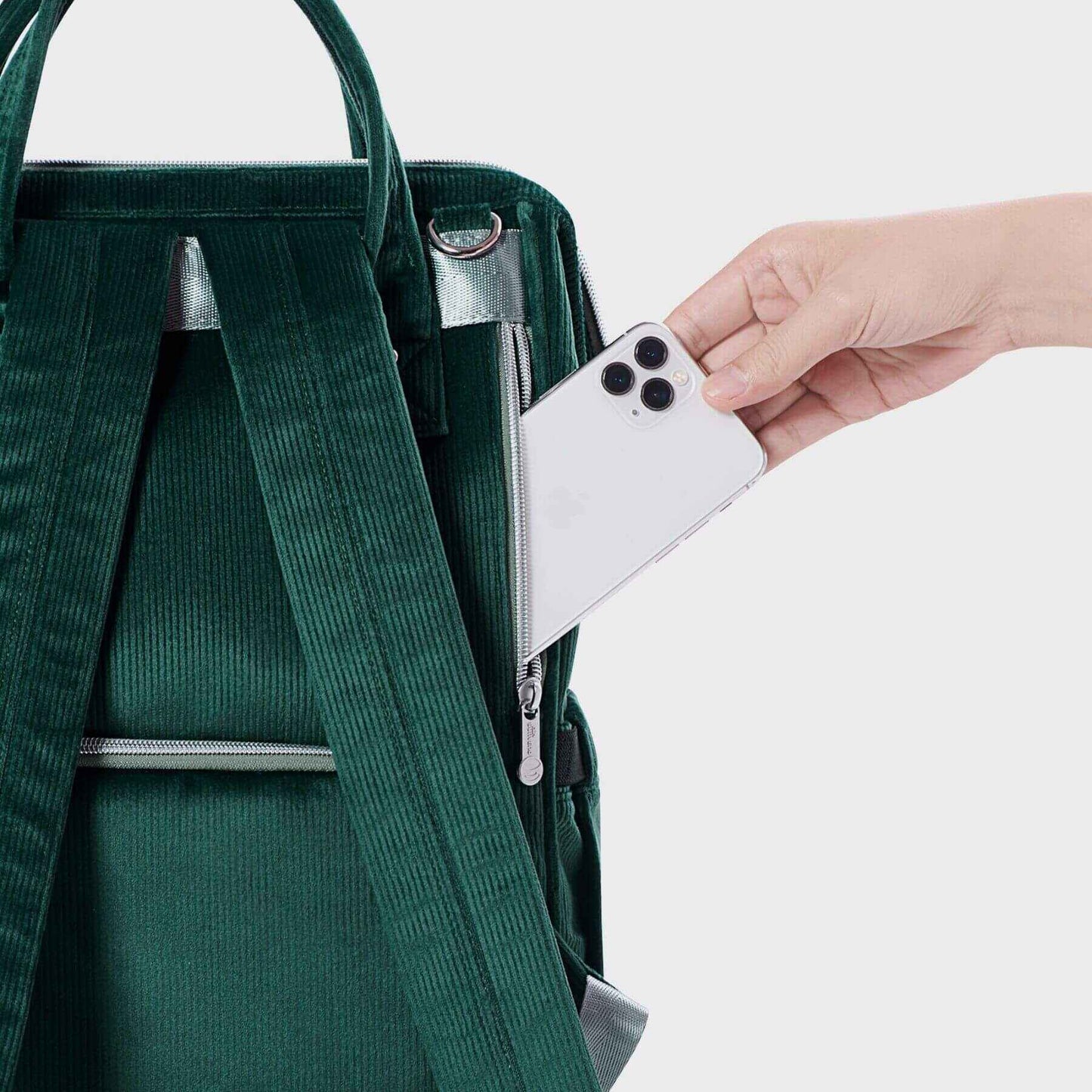 Corduroy Diaper Backpack Green with a hand reaching in to place a white phone inside.