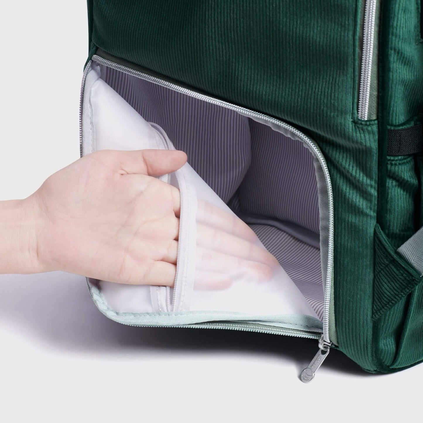 Corduroy Diaper Backpack Green with a hand placing a white garment inside