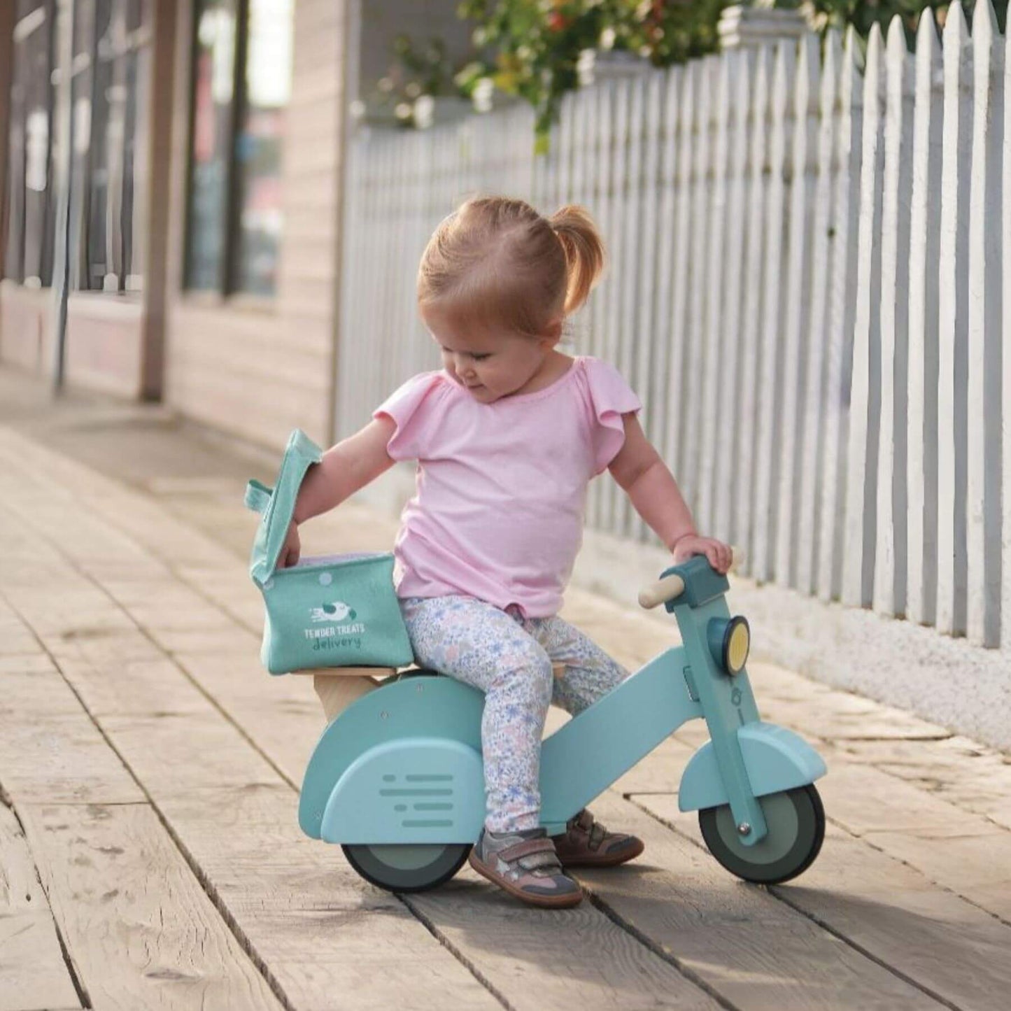 Child riding Tender Leaf Delivery Scooter on a wooden path.