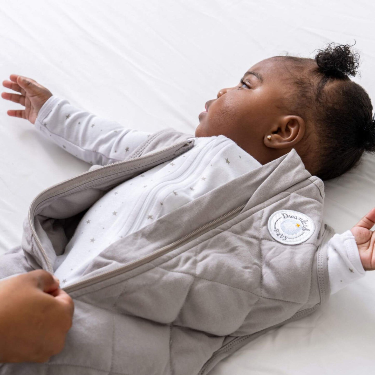 Baby lying on a white blanket wearing Dreamland Baby Dream Weighted Sleep Sack Moon Grey