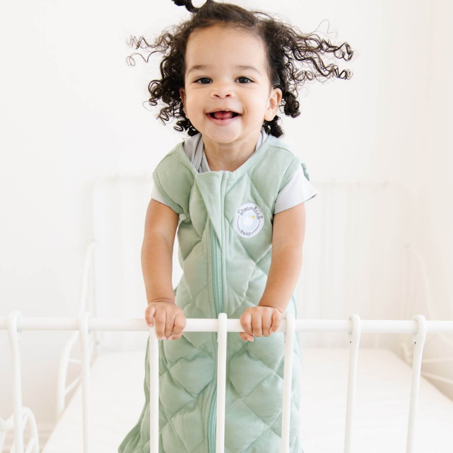 Child wearing Dreamland Baby Dream Weighted Sleep Sack Sage Green, standing in a crib.