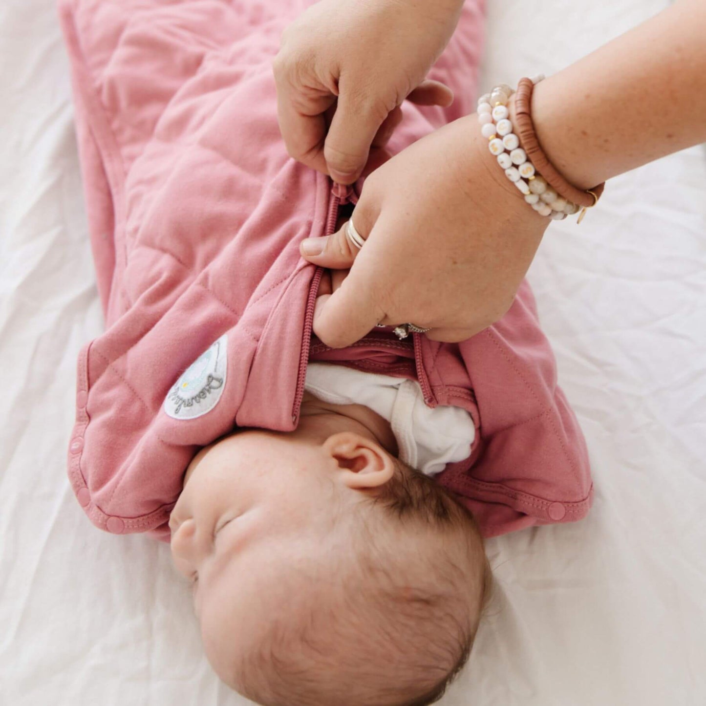 Baby in Dream Weighted Sleep Swaddle - Rose being adjusted by an adult on a white surface