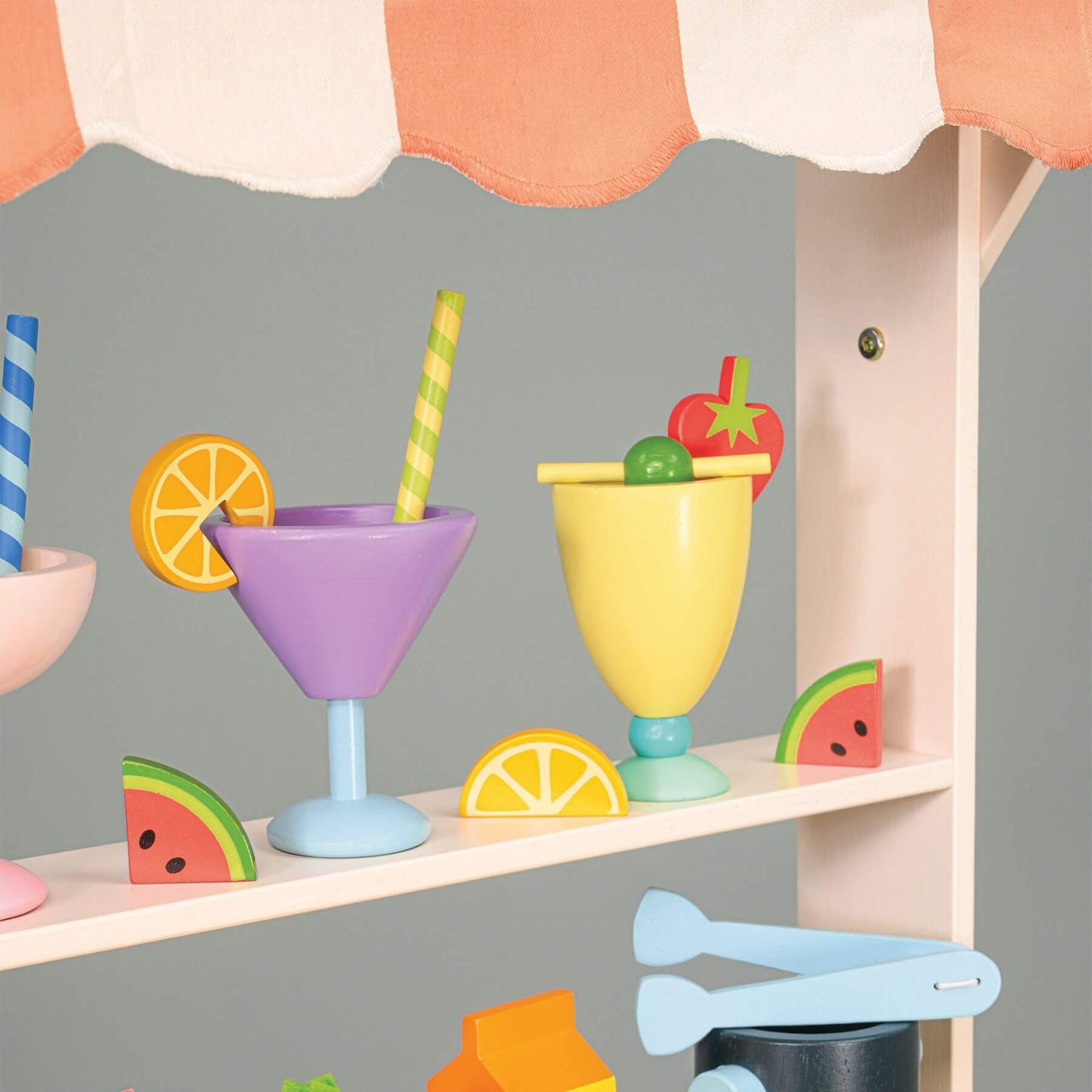 Colorful toy drink set with glasses, lemons, and a straw on a shelf against a gray background.
