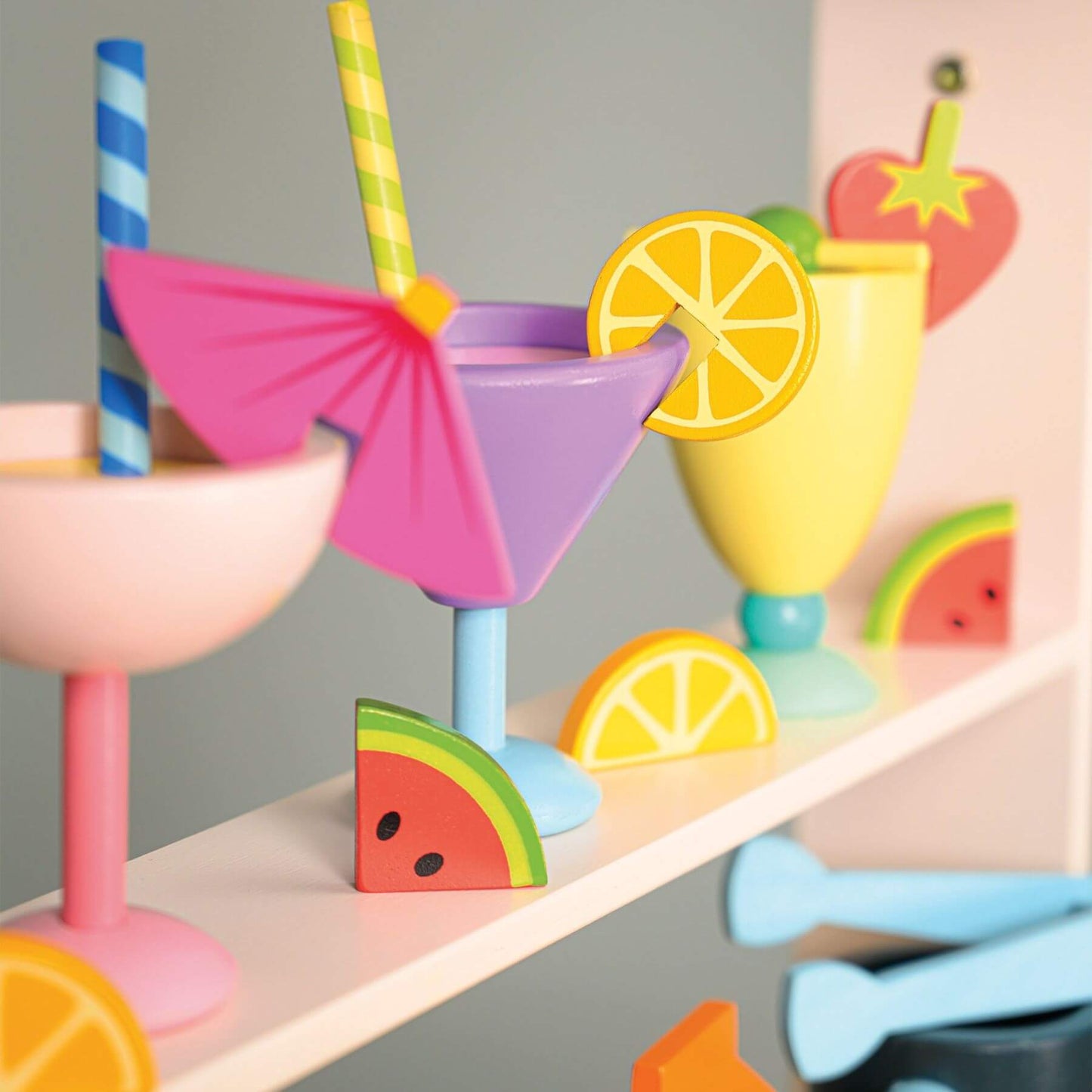 Colorful toy drink set with cups, straws, and fruit slices on a shelf.