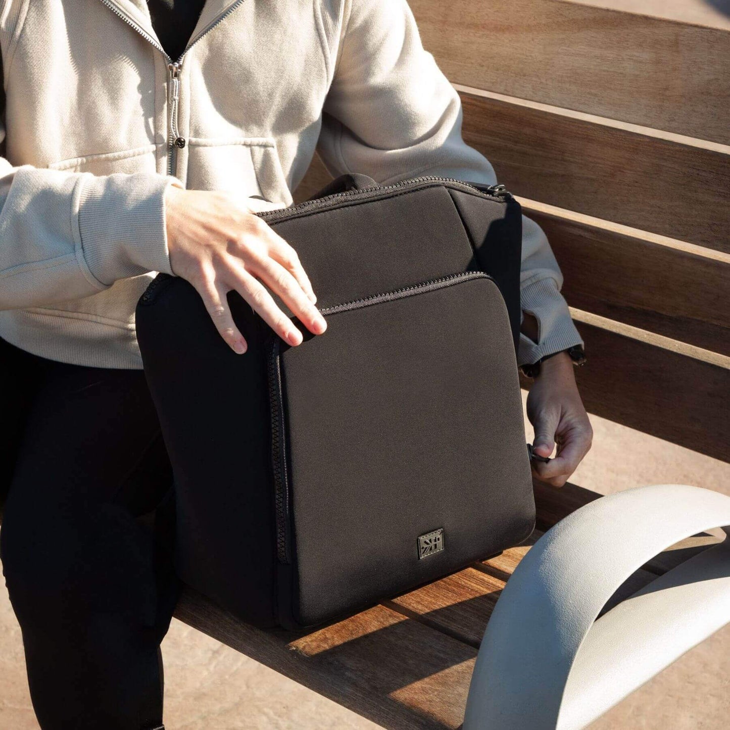 Person holding Ebony Seoul Neoprene Backpack II on a wooden surface