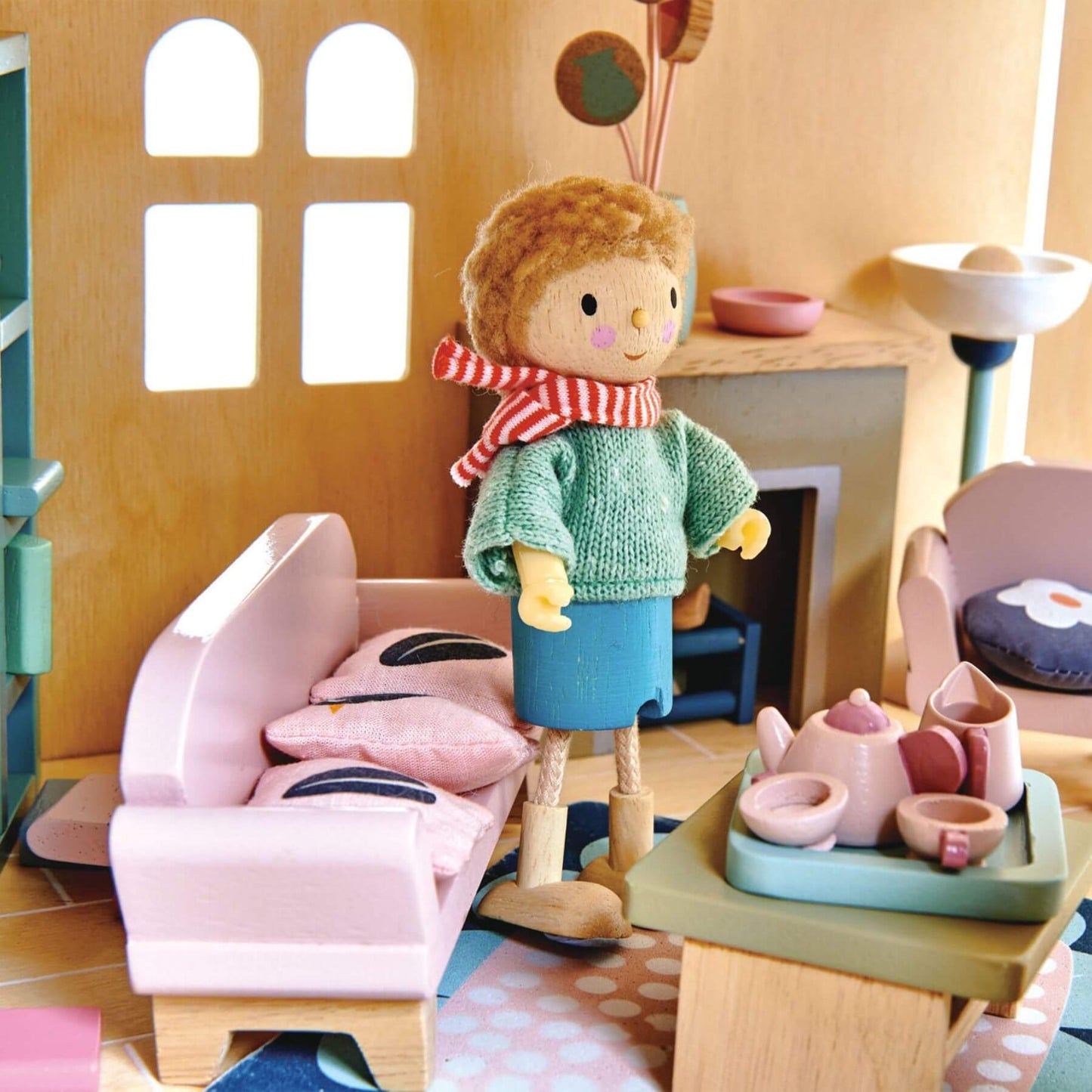 Toy doll with a striped scarf standing in a playroom with furniture and toys.