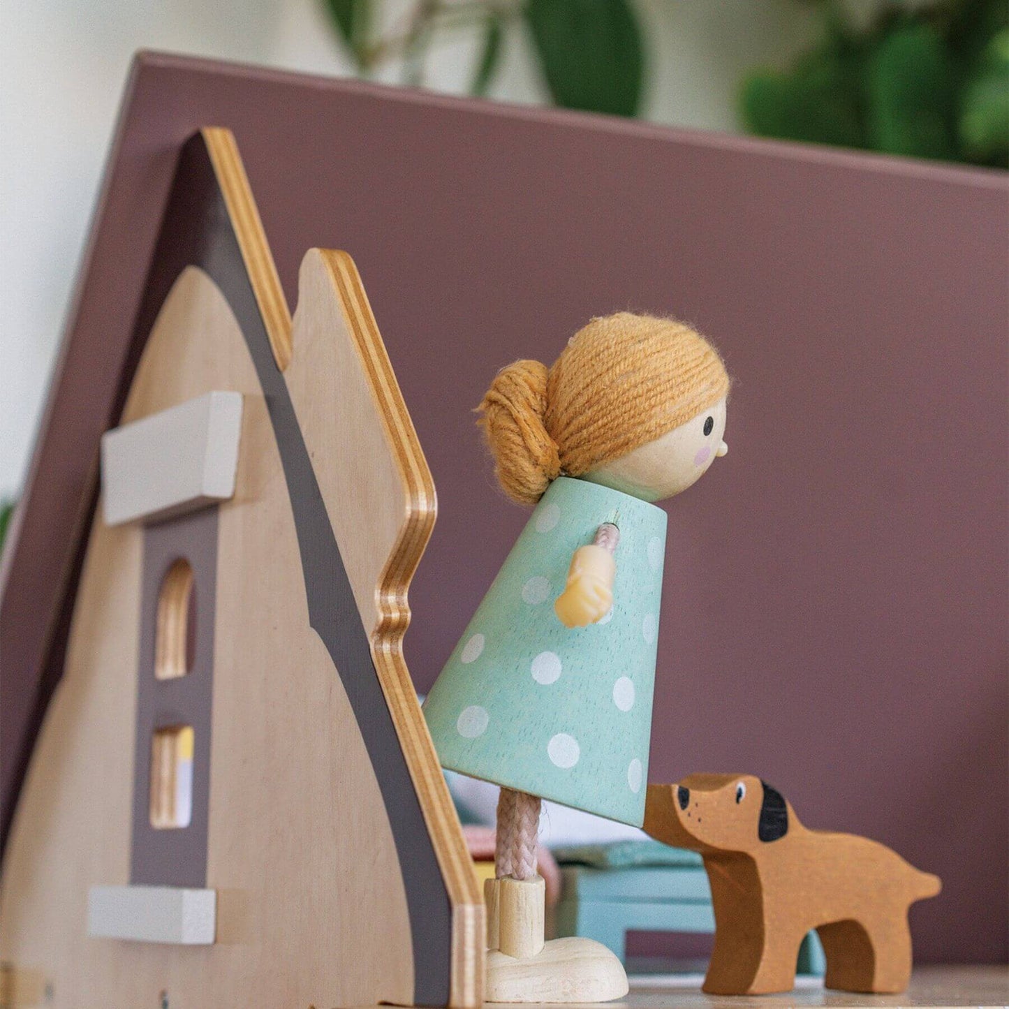 Wooden toy house with a girl figurine and a dog in front of a purple background