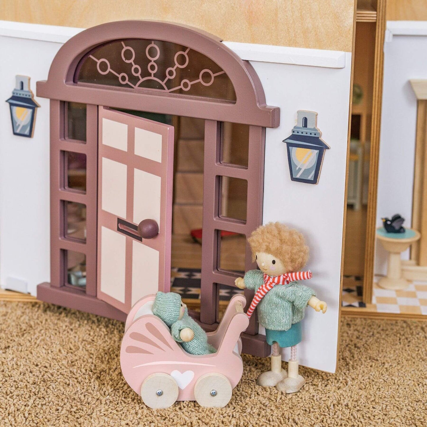 Dolls and a baby carriage in front of a dollhouse door with a lamp post.