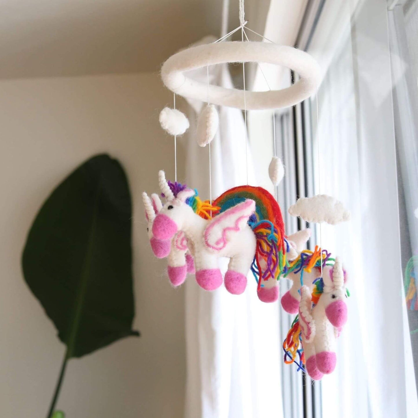 Ganapati Crafts Co. Felt Unicorn Baby Mobile hanging in a room with a window in the background