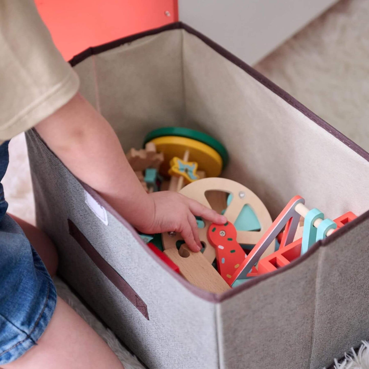 Child playing with colorful wooden toys inside a gray storage bin.