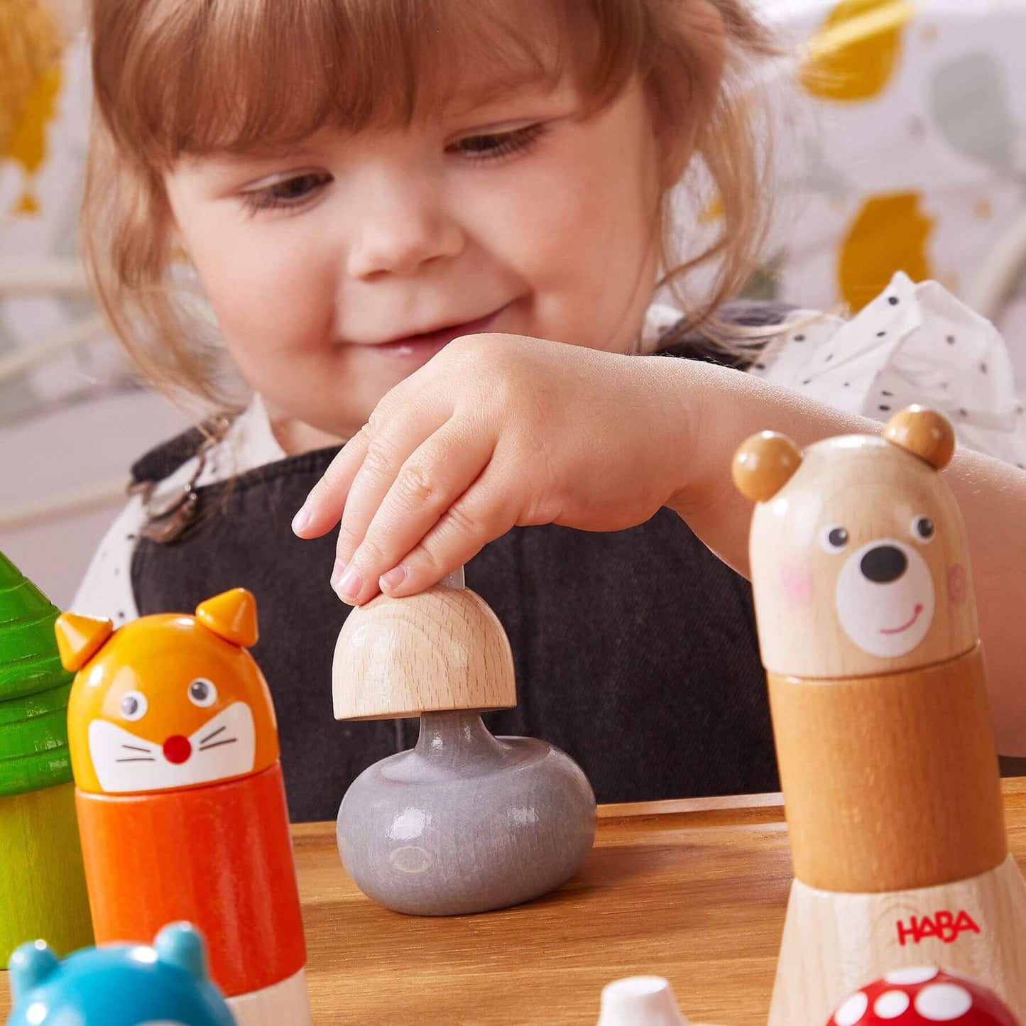 Child playing with HABA USA Forest Animals Wooden Stacking Toy on a wooden table.