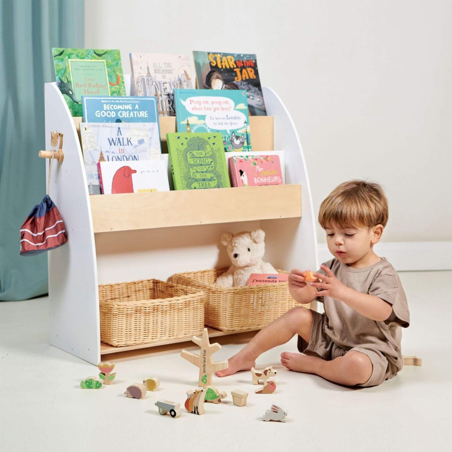Child playing with toys in front of Tender Leaf Forest Book Case filled with books and toys.