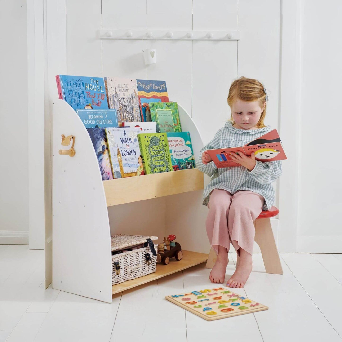 Child reading a book next to Tender Leaf Forest Book Case with books on a white floor.