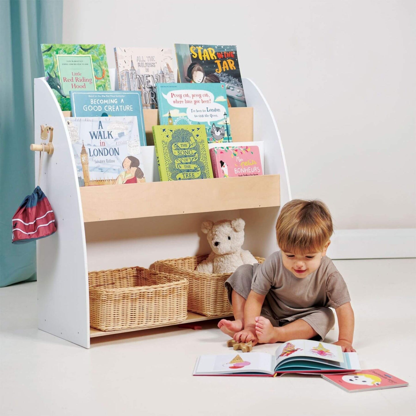 Child sitting on the floor reading a book next to Tender Leaf Forest Book Case with books and toys.