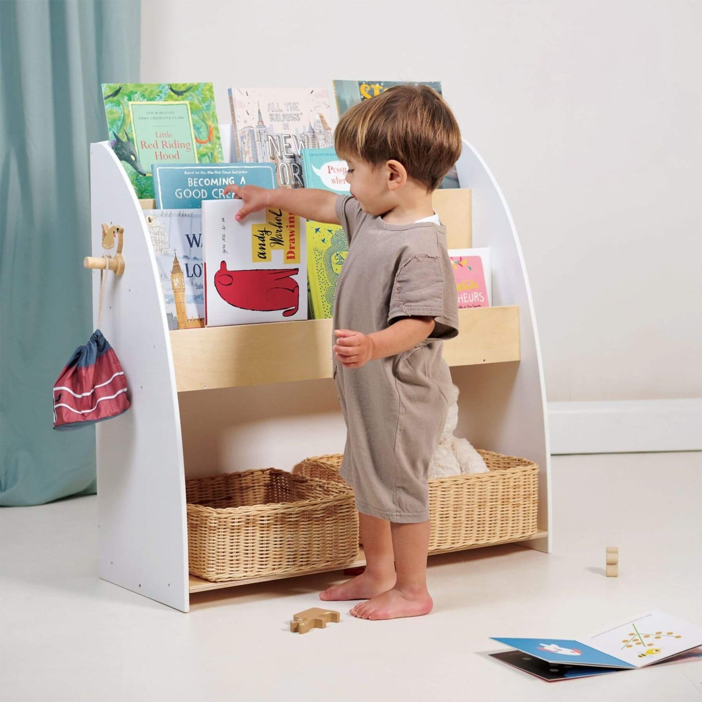 Child interacting with Tender Leaf Forest Book Case filled with books on a light-colored floor.