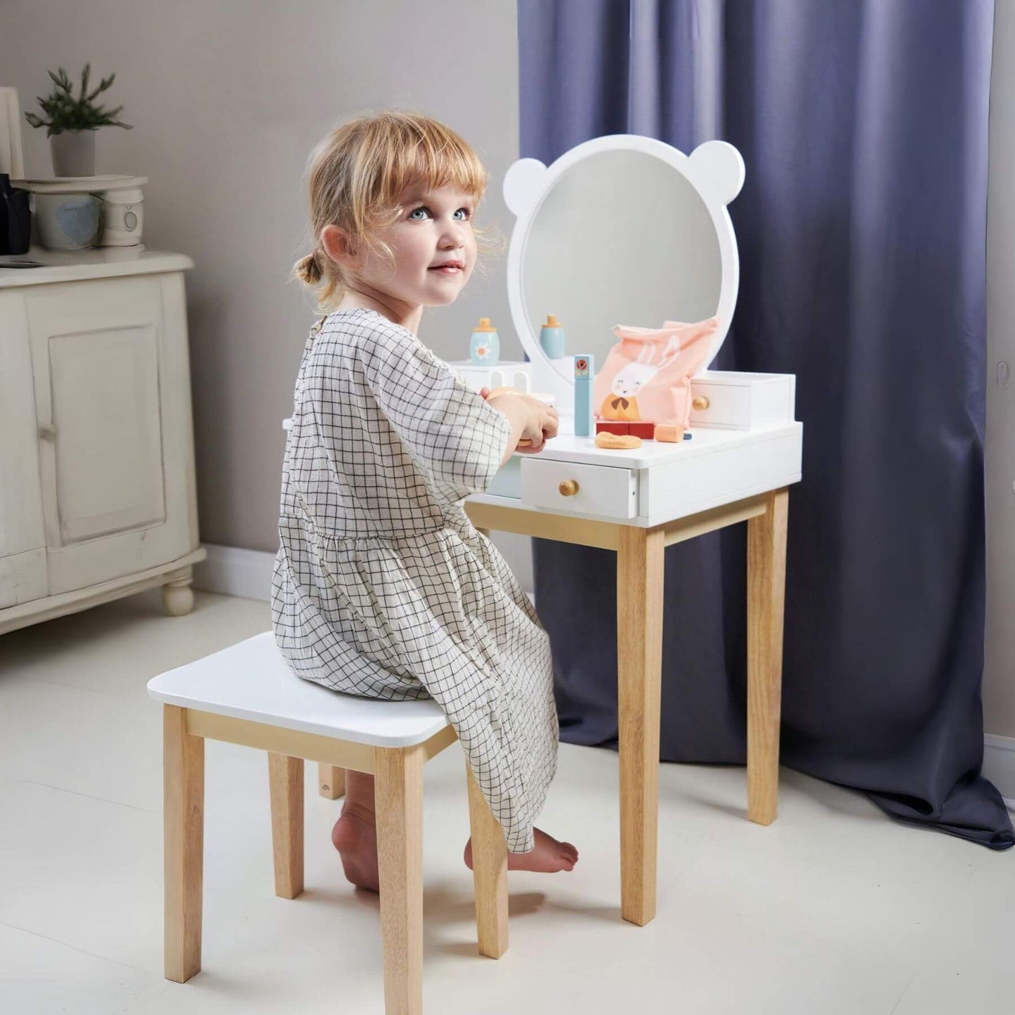 Child sitting at Tender Leaf Forest Dressing Table and various items in a room.