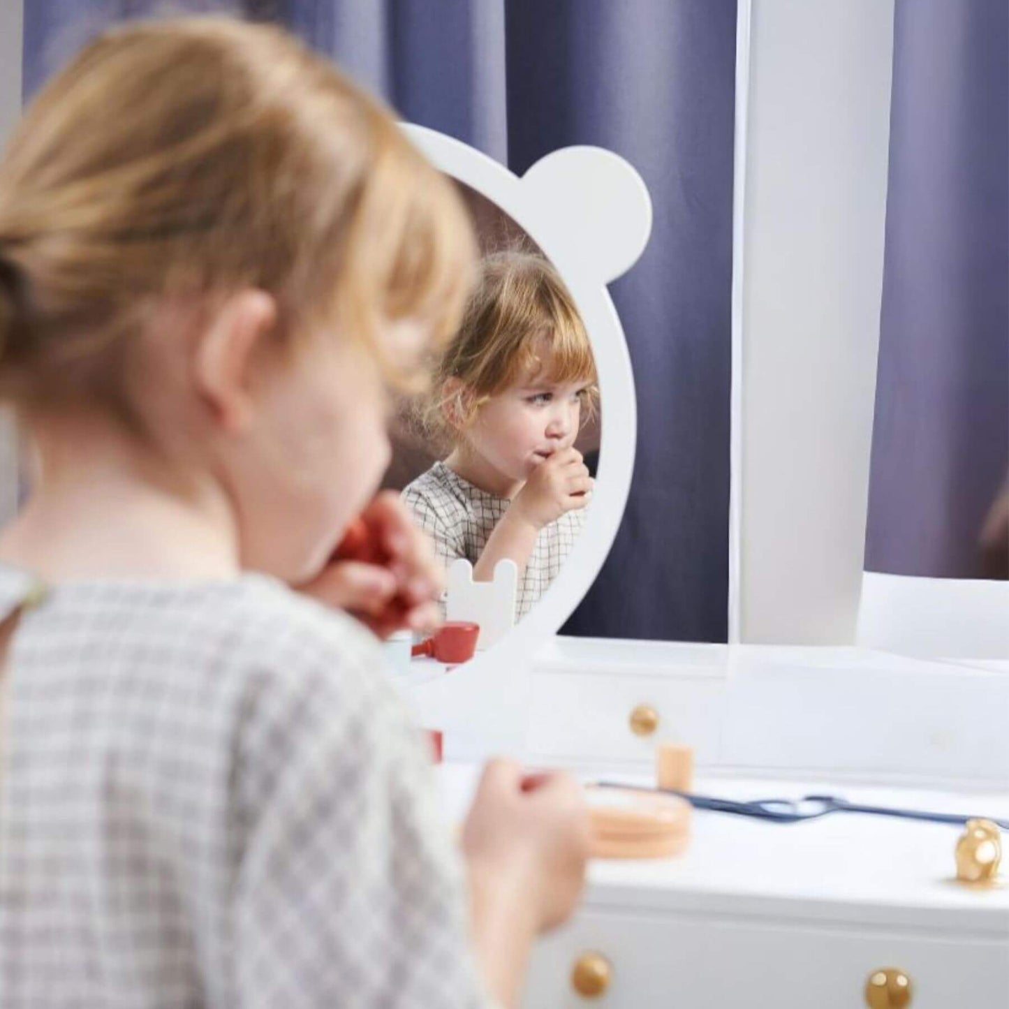 Child looking at themselves in a mirror with a striped curtain in the background