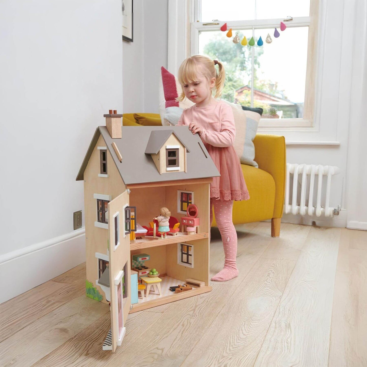 Child playing with Tender Leaf Foxtail Villa in a bright room with a yellow chair and window.