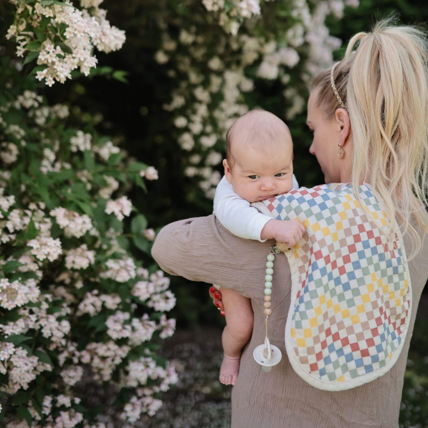 Woman holding a baby wrapped in a colorful blanket with flowers in the background