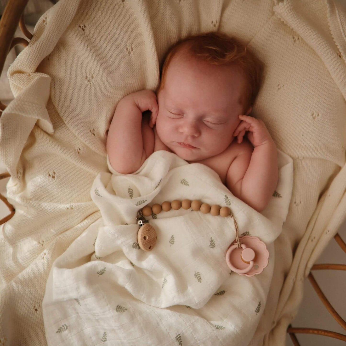 Newborn baby sleeping in a basket with a white blanket and FRIGG pacifier.