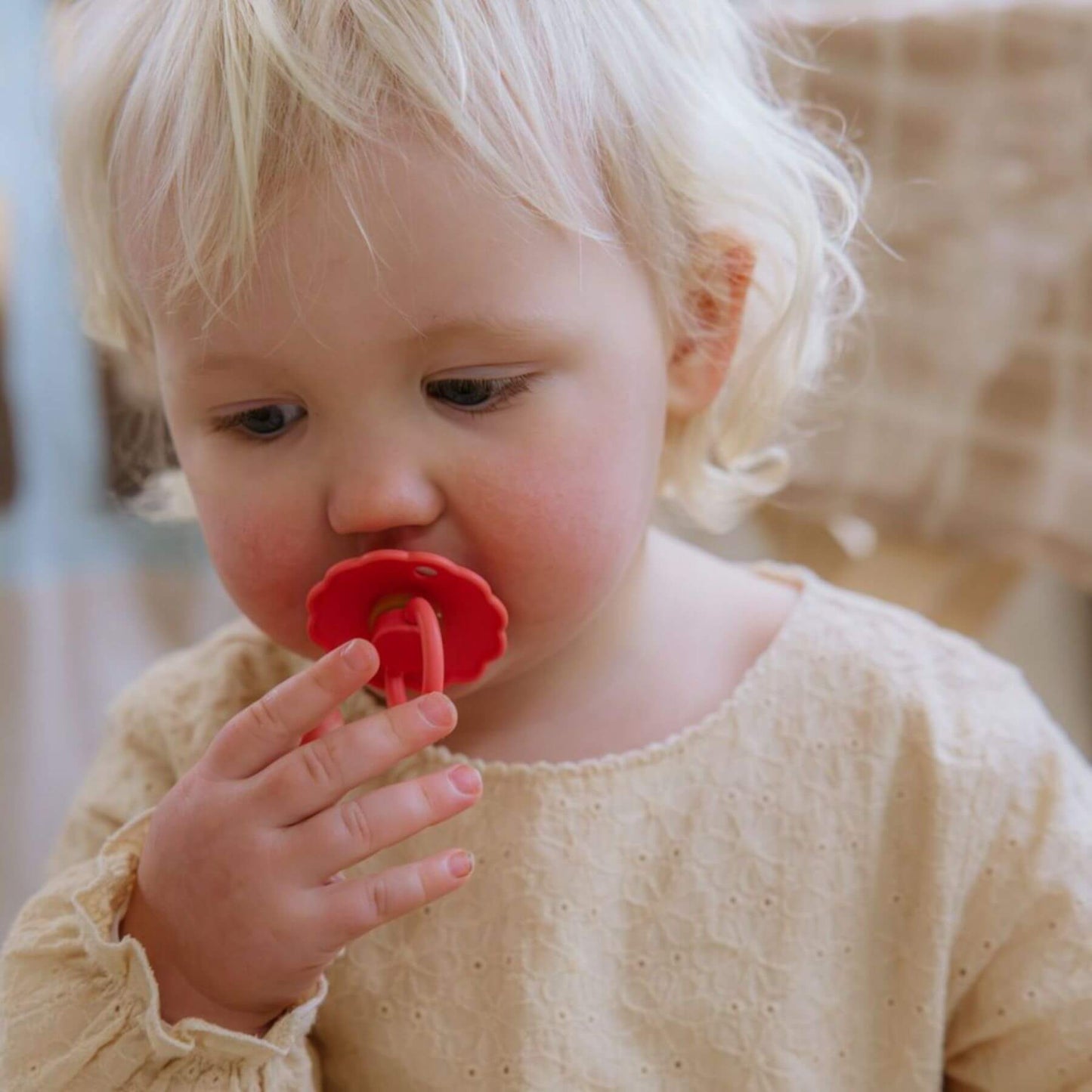Child holding a FRIGG pacifier near their mouth with a blurred background