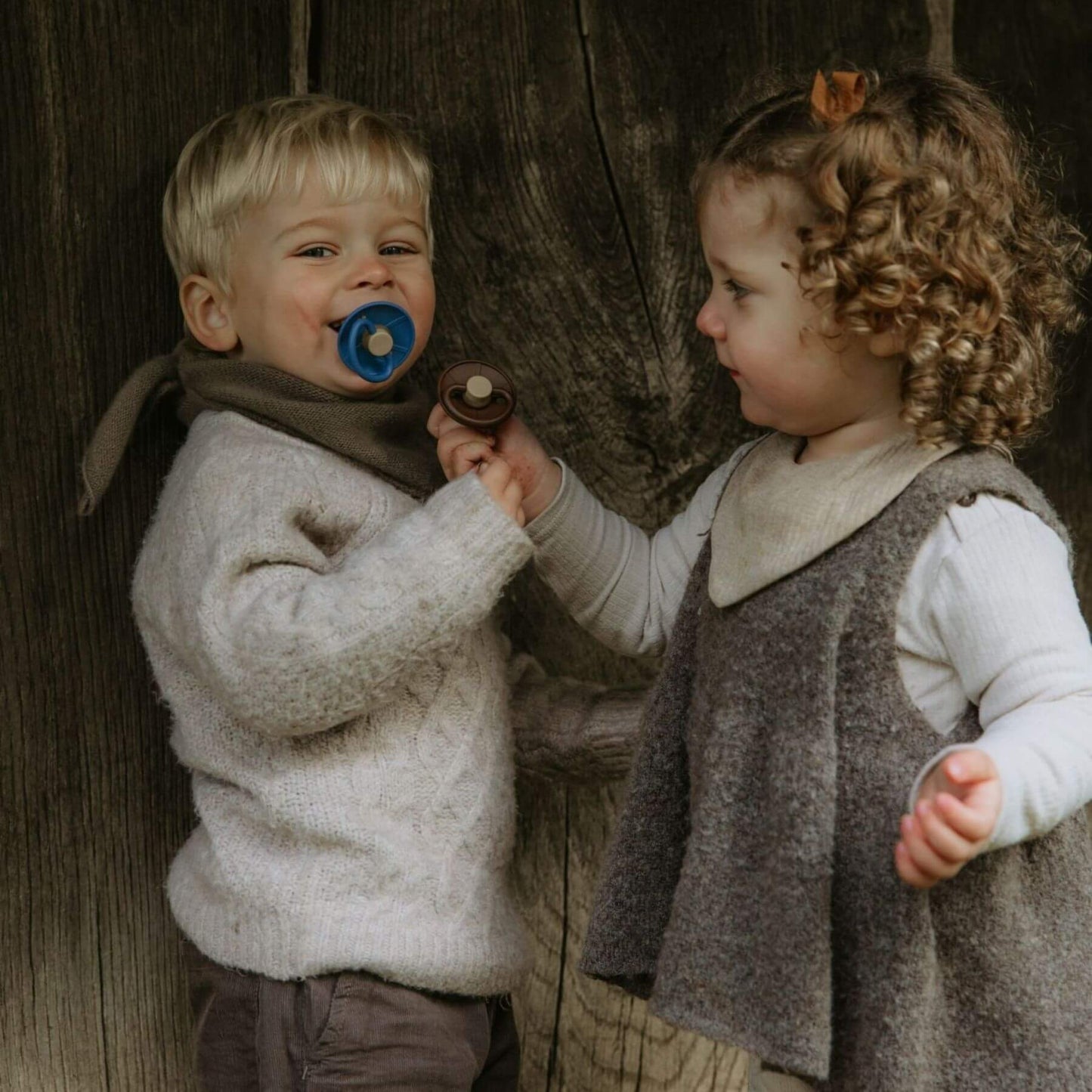 Two children in vintage clothing standing next to a wooden wall.