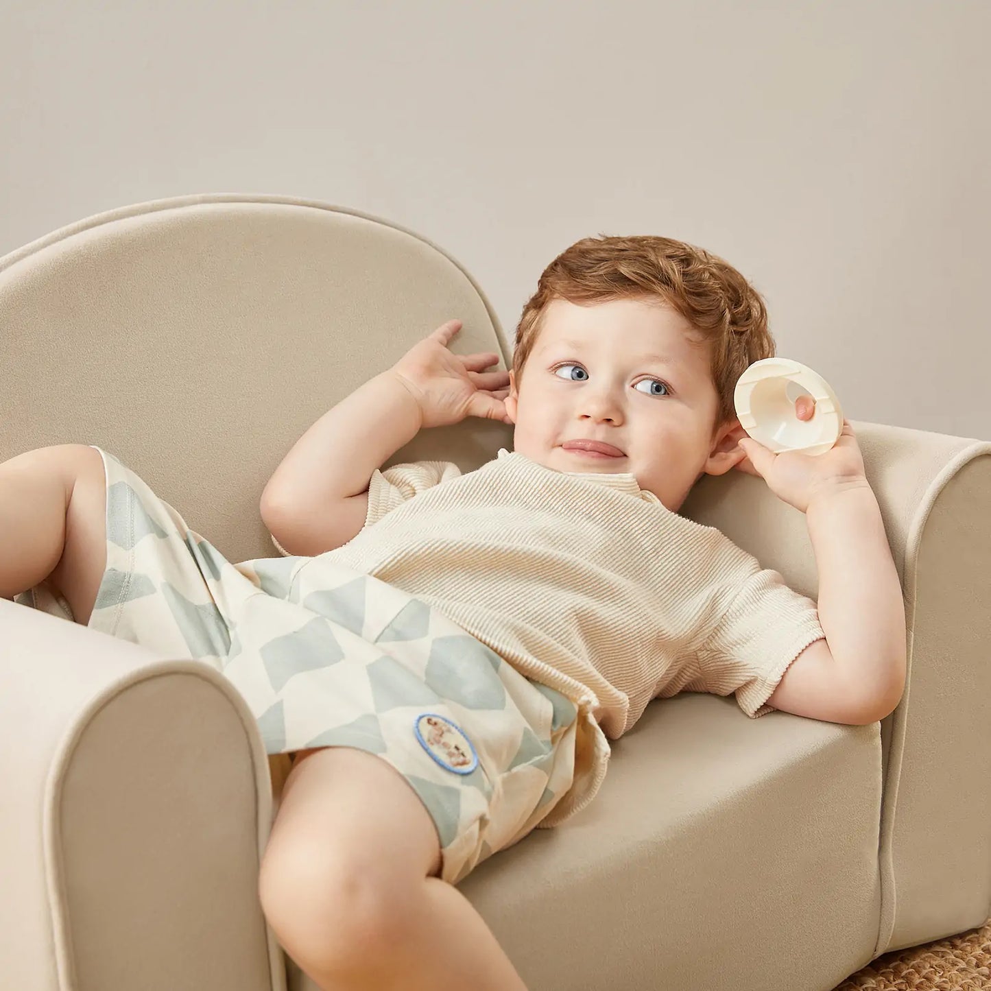Child lying on Tiny Land® GentleSnug Kid Chair Beige White holding a small object