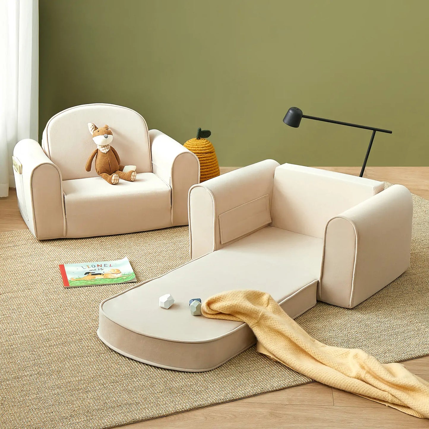 Tiny Land® GentleSnug Kid Chair Beige White with toys and a book on a wooden floor against a green wall.