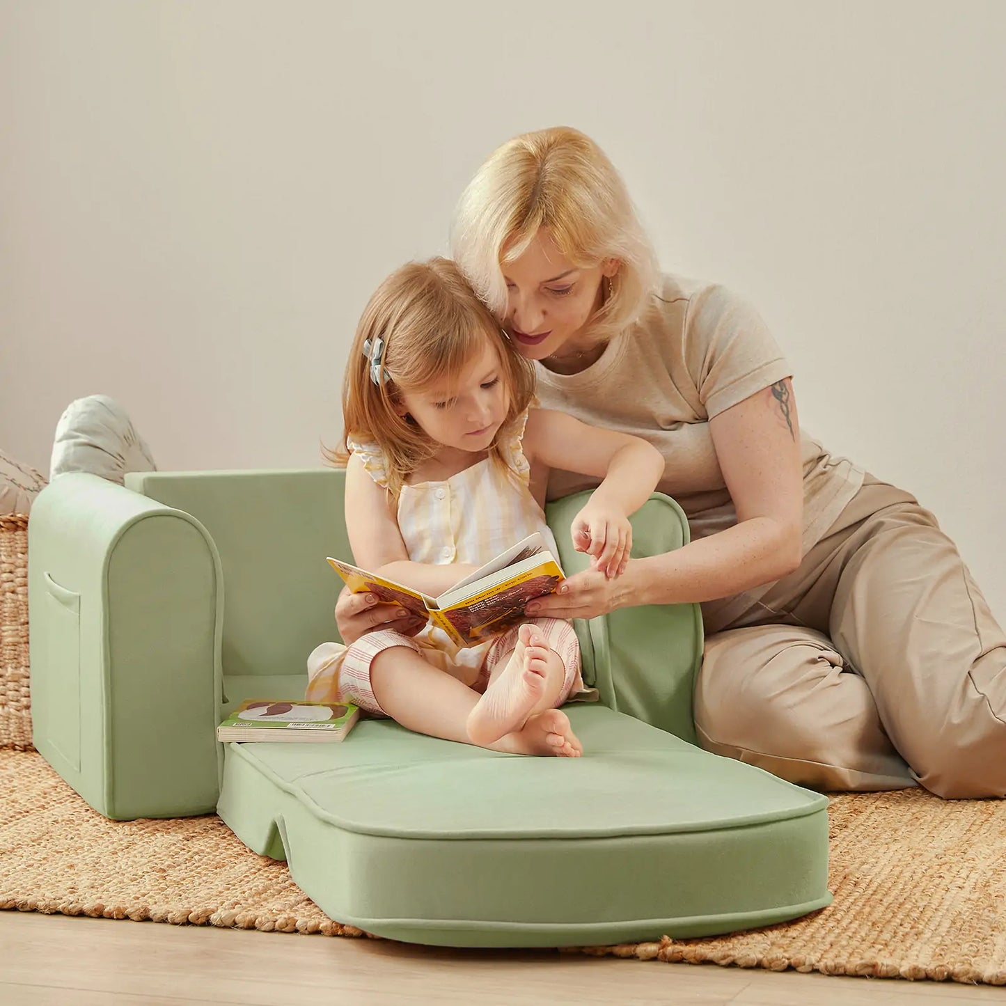 Woman and child sitting on Tiny Land® GentleSnug Kid Chair Sage reading a book together.
