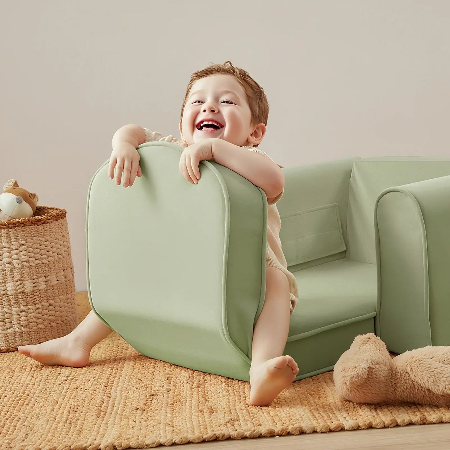 Child playing with Tiny Land® GentleSnug Kid Chair Sage on a couch in a cozy room.