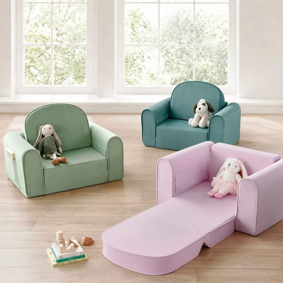 Three Tiny Land® GentleSnug Kids Sofa Chairs are arranged on a light wood floor in a bright room with large windows.