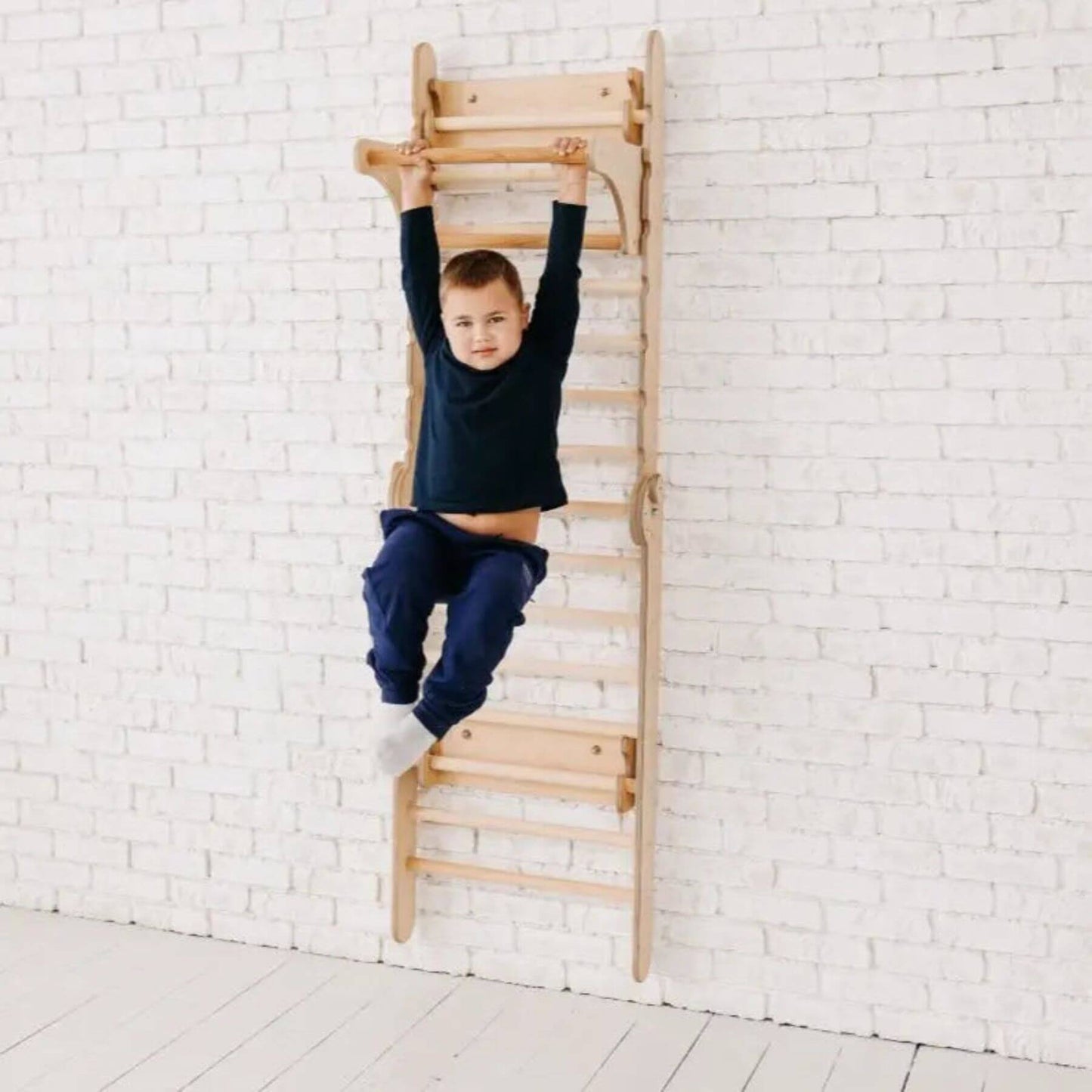 Child climbing a wooden wall climber against a white brick wall.