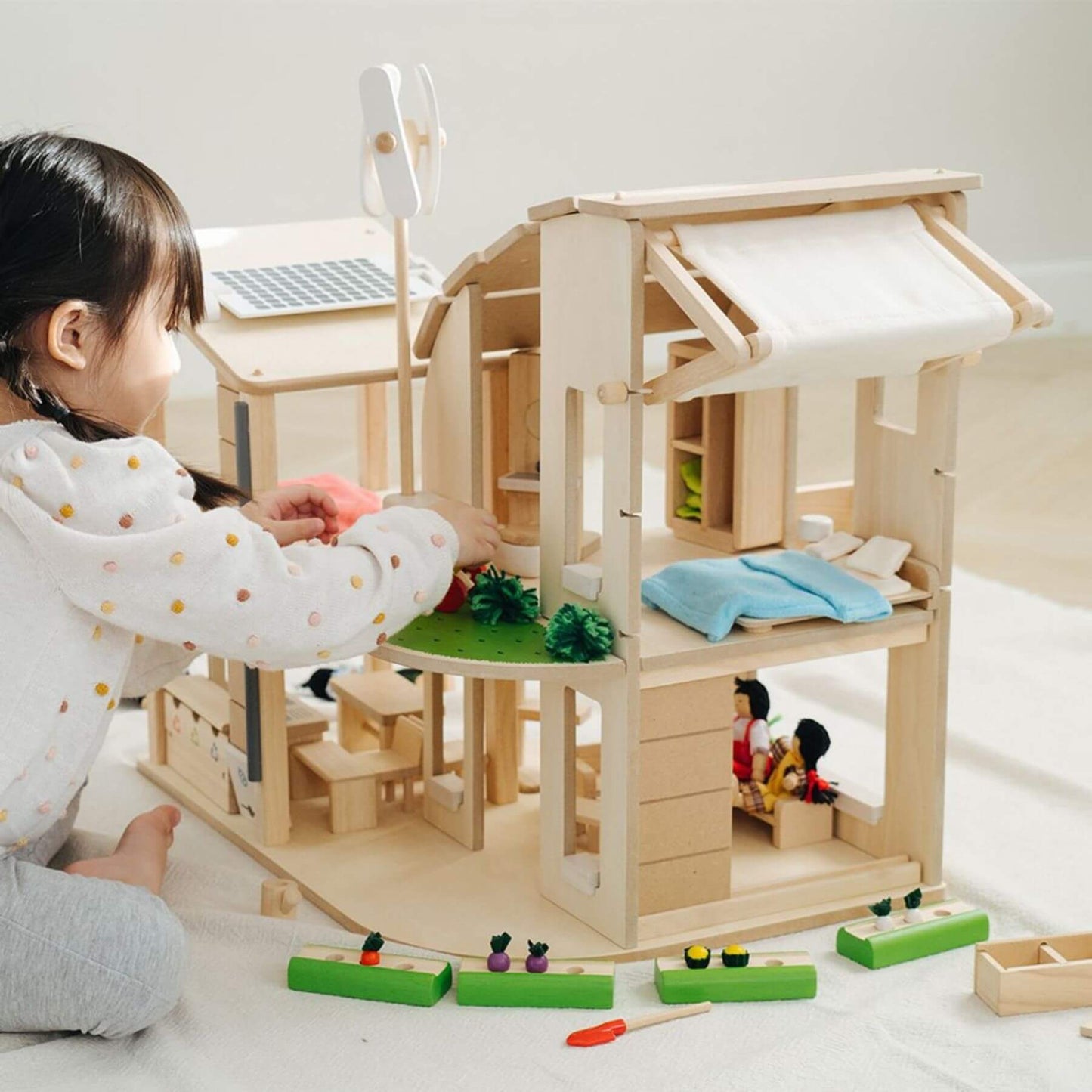 Child playing with PlanToys Green Dollhouse With Furniture on a light-colored floor.
