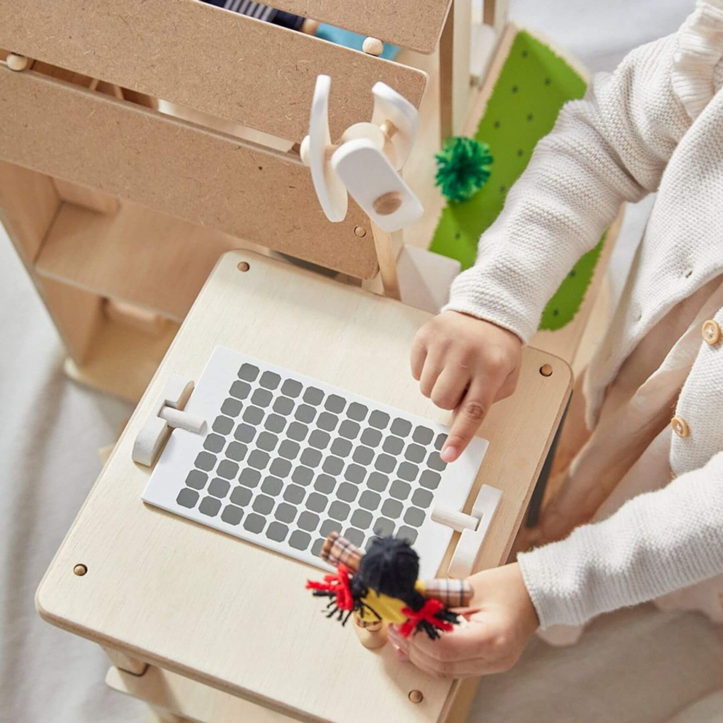 Child playing with PlanToys Green Dollhouse With Furniture on a wooden table