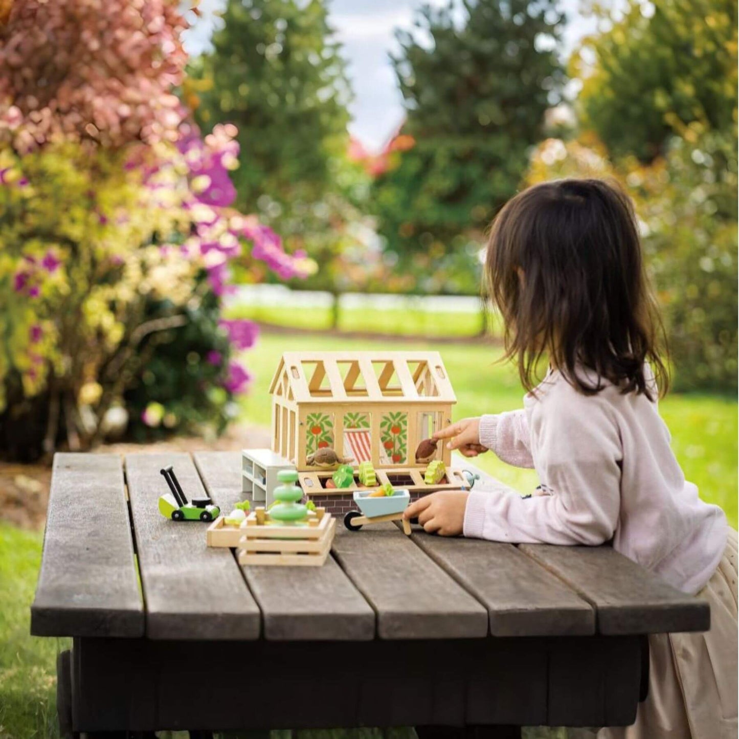 Child playing with Tender Leaf Greenhouse and Garden Set on a wooden table outdoors