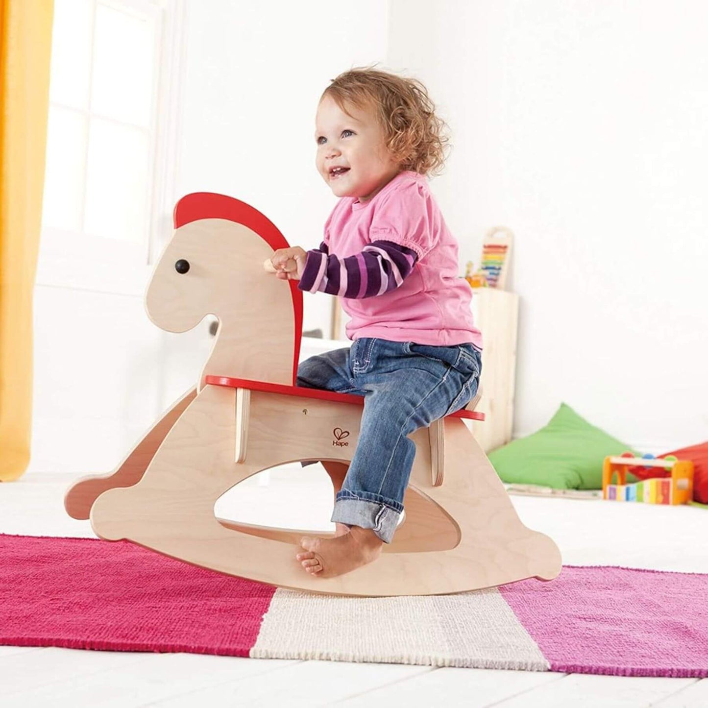 Child sitting on Hape Grow-with-me Rocking Horse in a bright room with colorful toys.