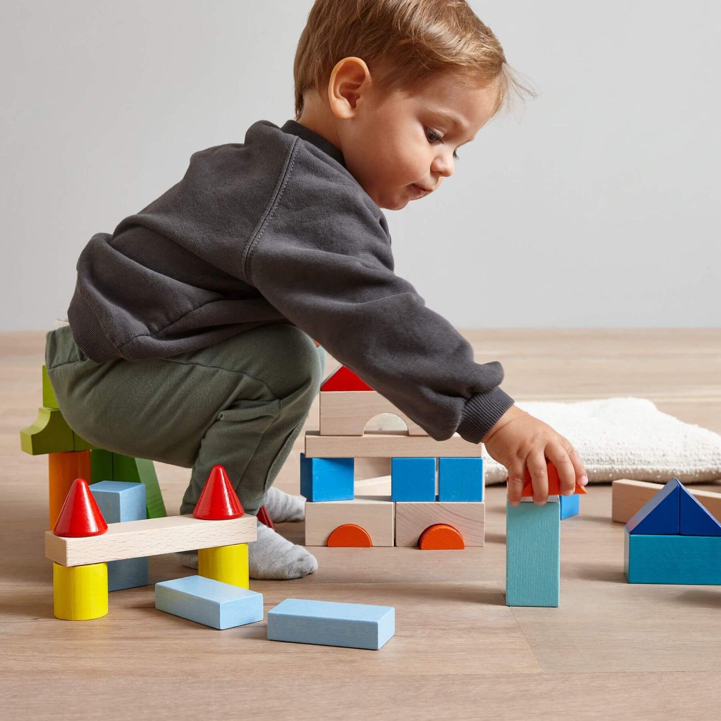 Child playing with HABA USA Colored Wooden Building Blocks - 46 Piece Set on a wooden floor