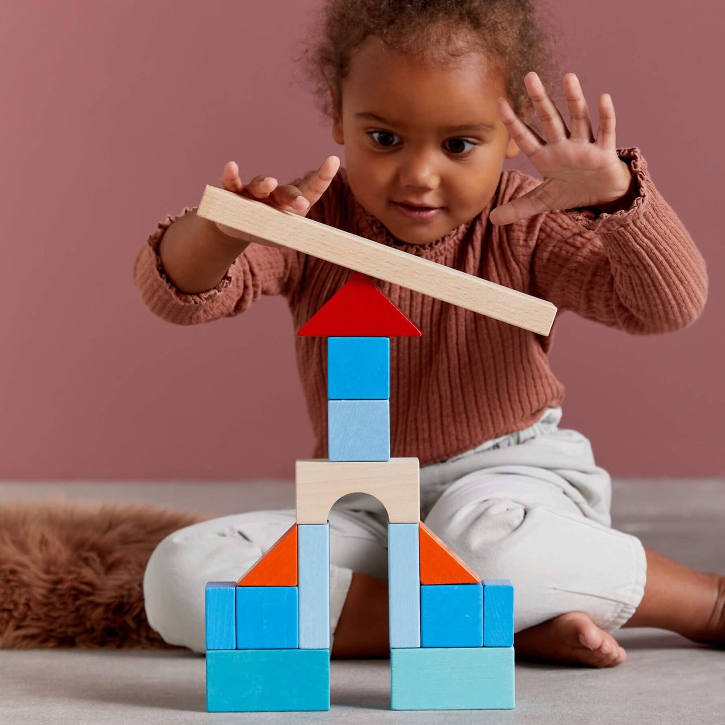 Child playing with wooden blocks against a pink background