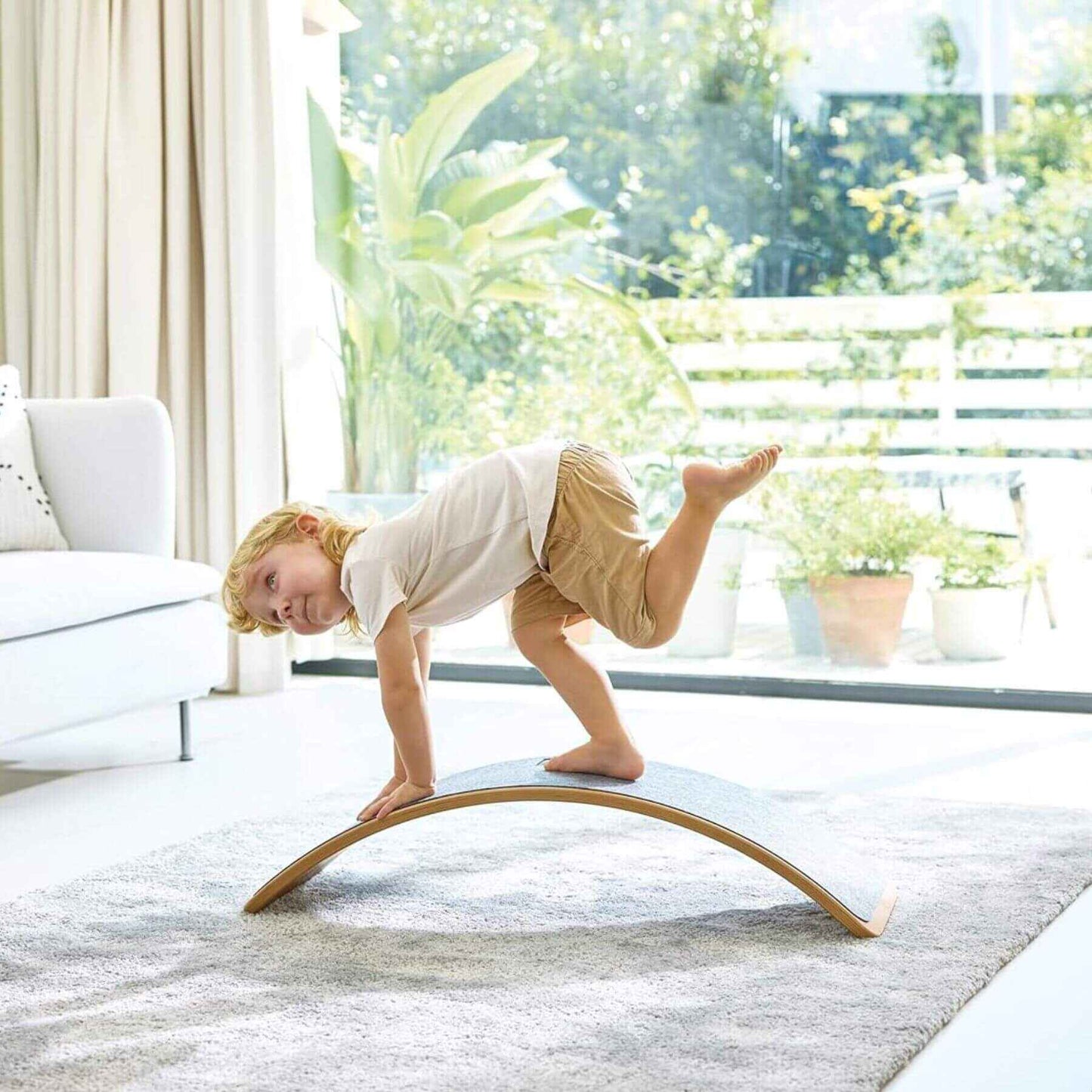 Child balancing on Hape Light Up Balance Board in a bright living room with large windows.