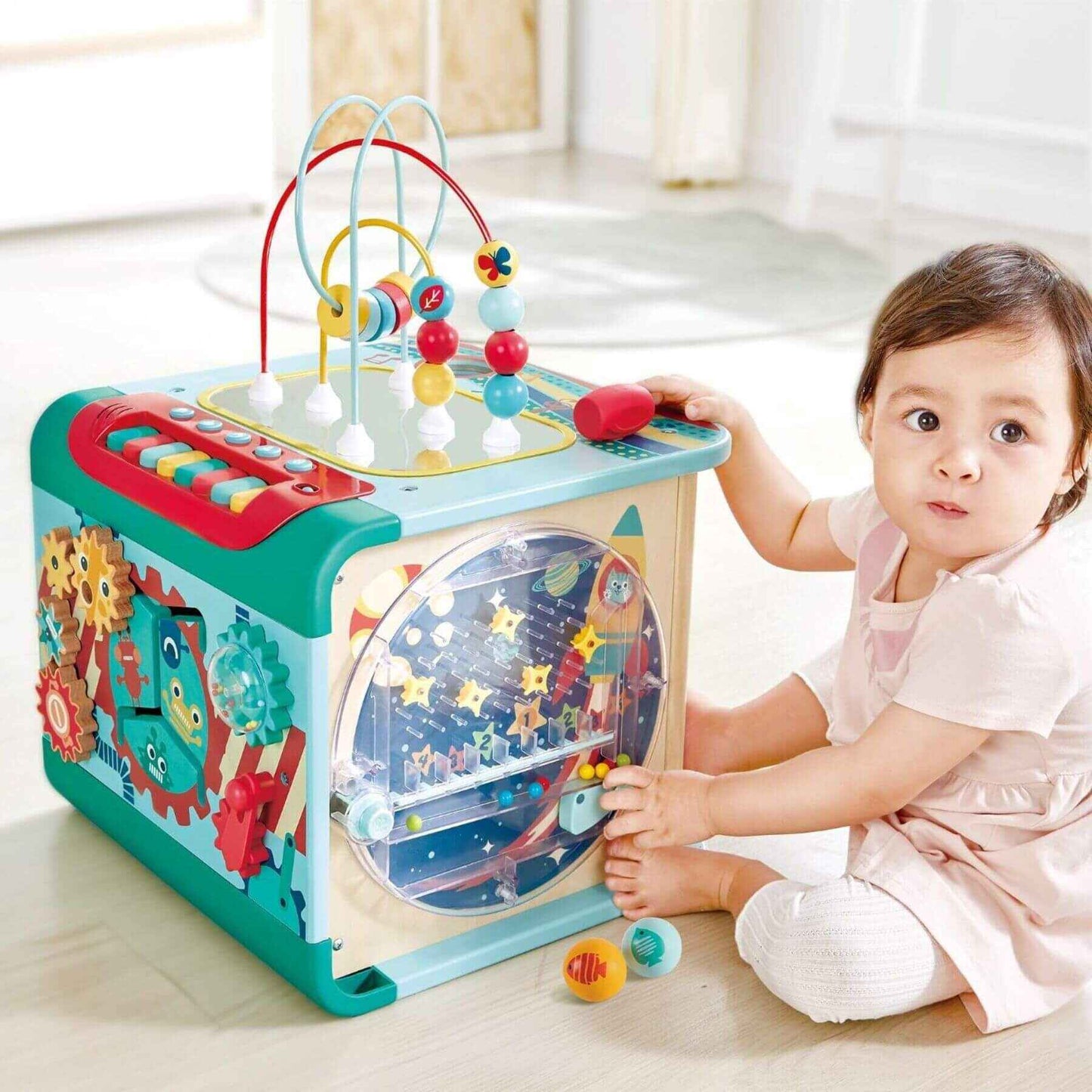 Child playing with Hape Explore and Learn Magic Cube on a light wooden floor.