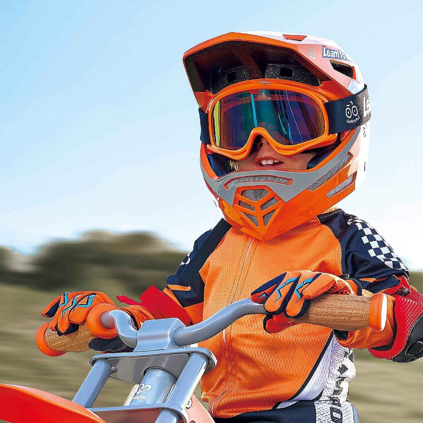 Child wearing Hape Sports Rider Safety Helmet and gear, sitting on a bike with a blurred natural background.