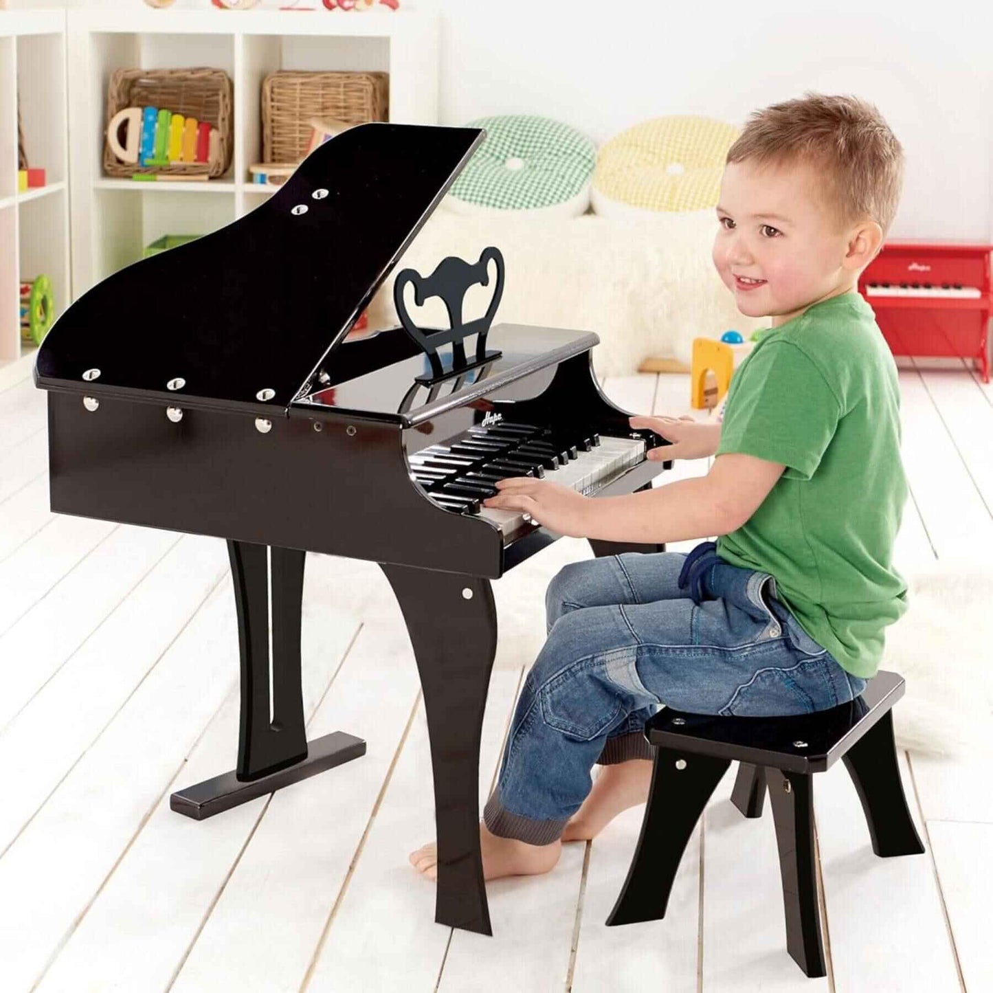 Child playing Hape Happy Grand Piano Black in a bright room with colorful toys in the background