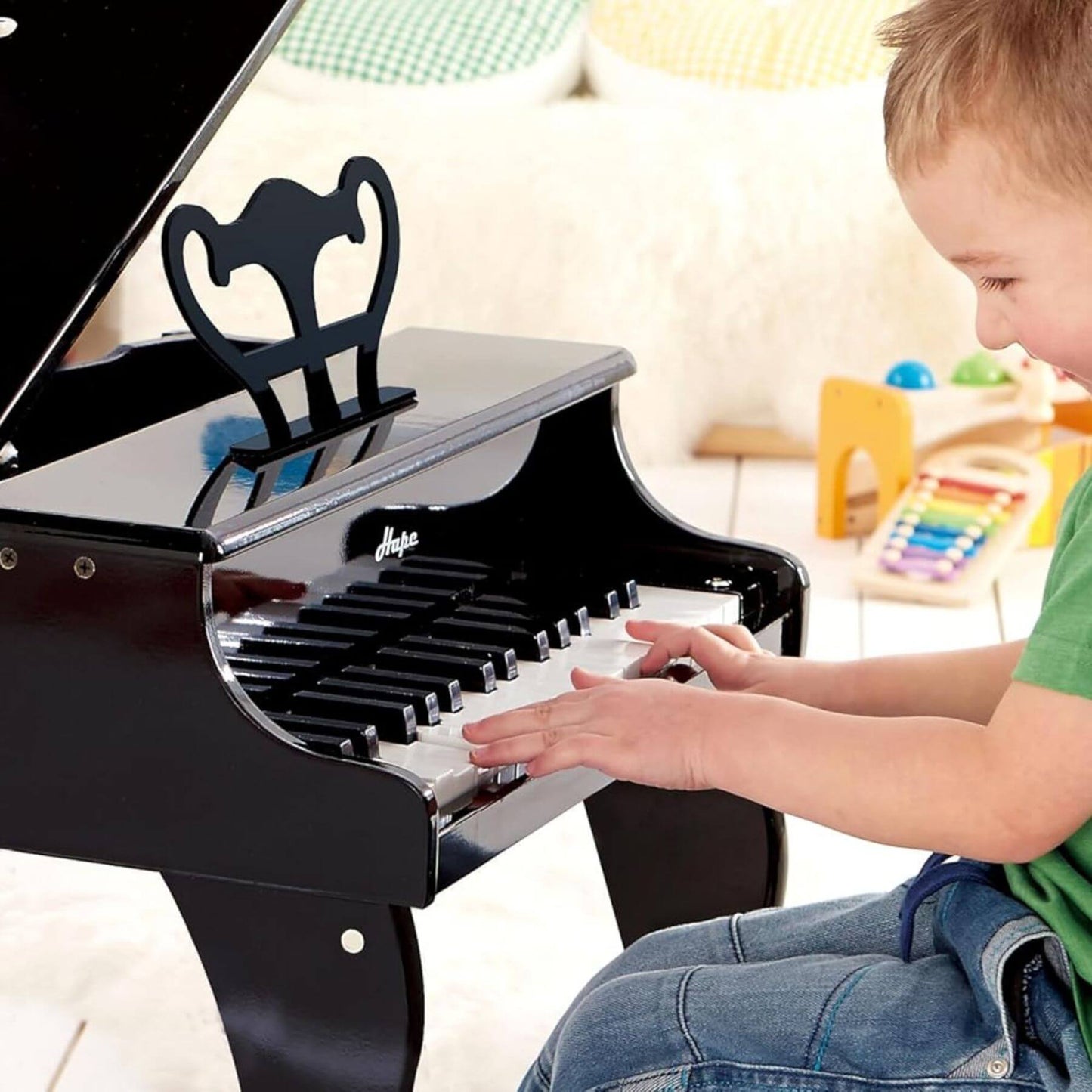 Child playing Hape Happy Grand Piano Black in a room with colorful toys in the background