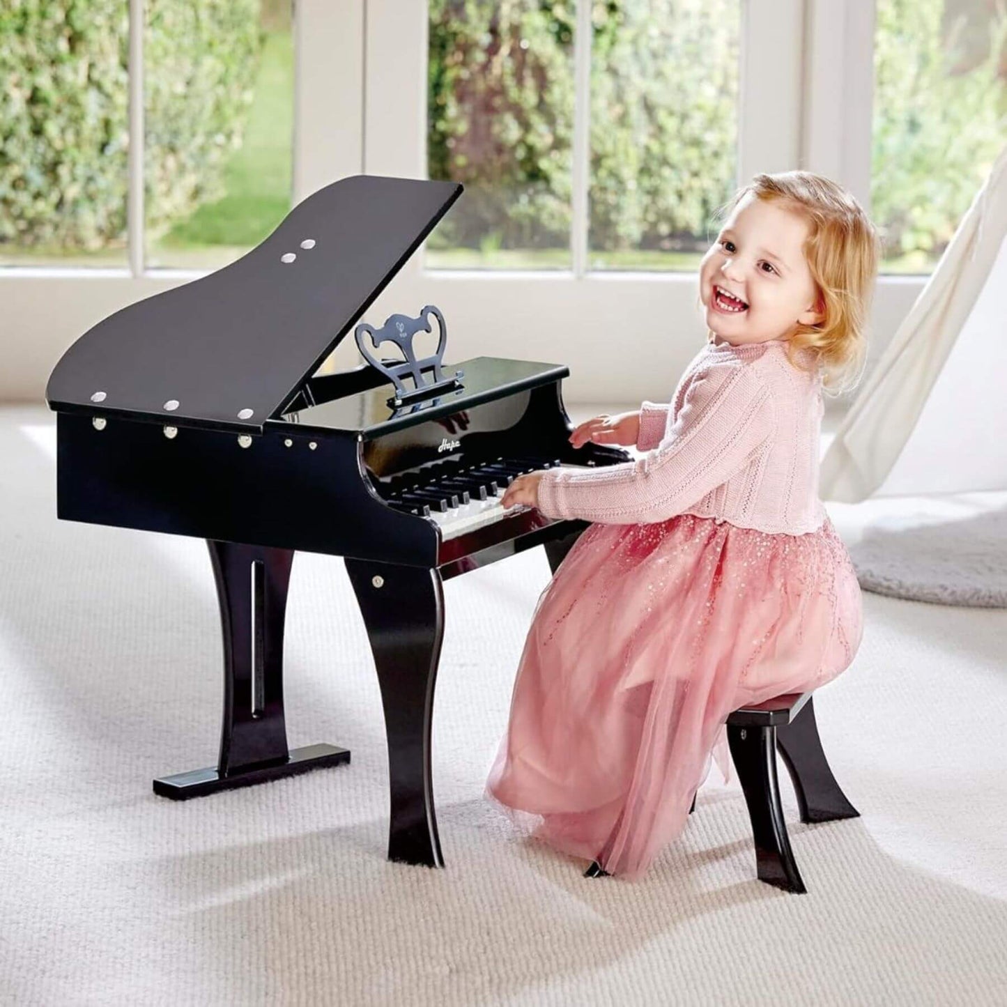 Child playing Hape Happy Grand Piano Black in a bright room with large windows.