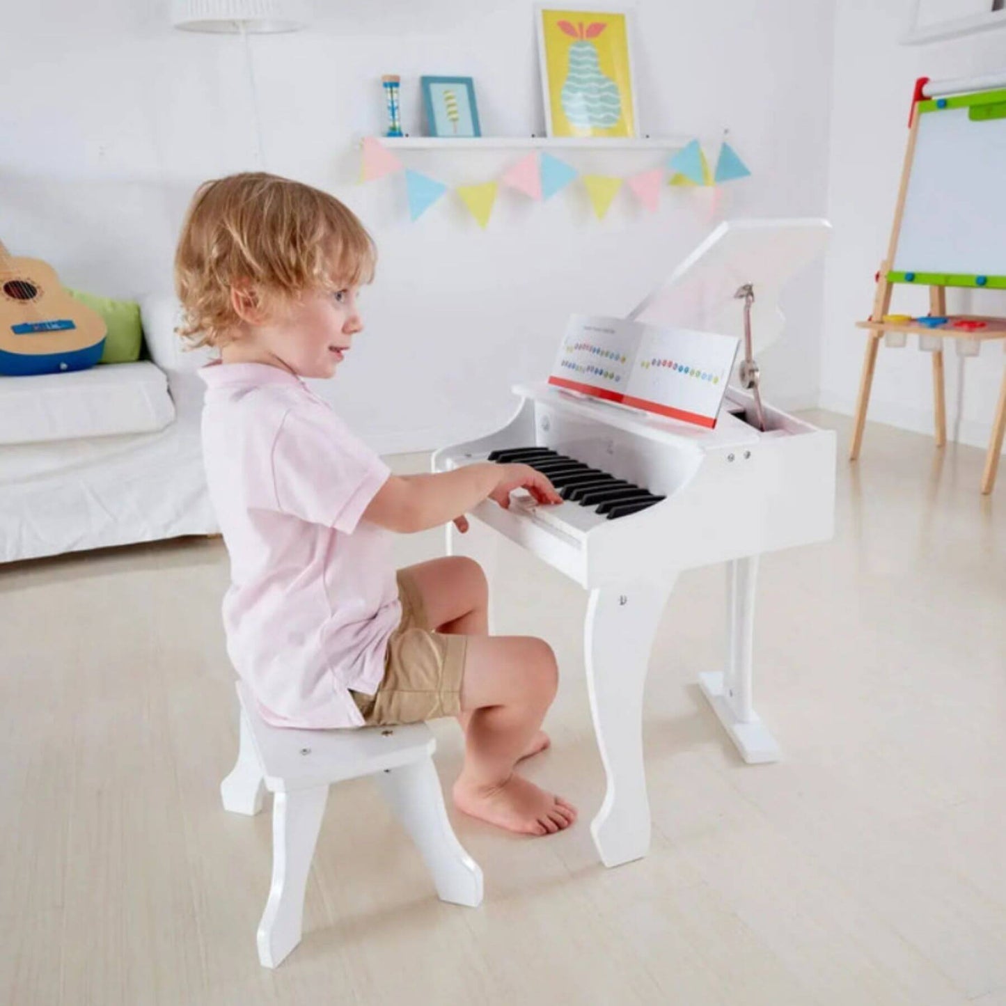 Child playing Hape Happy Grand Piano White in a bright room with toys and furniture.
