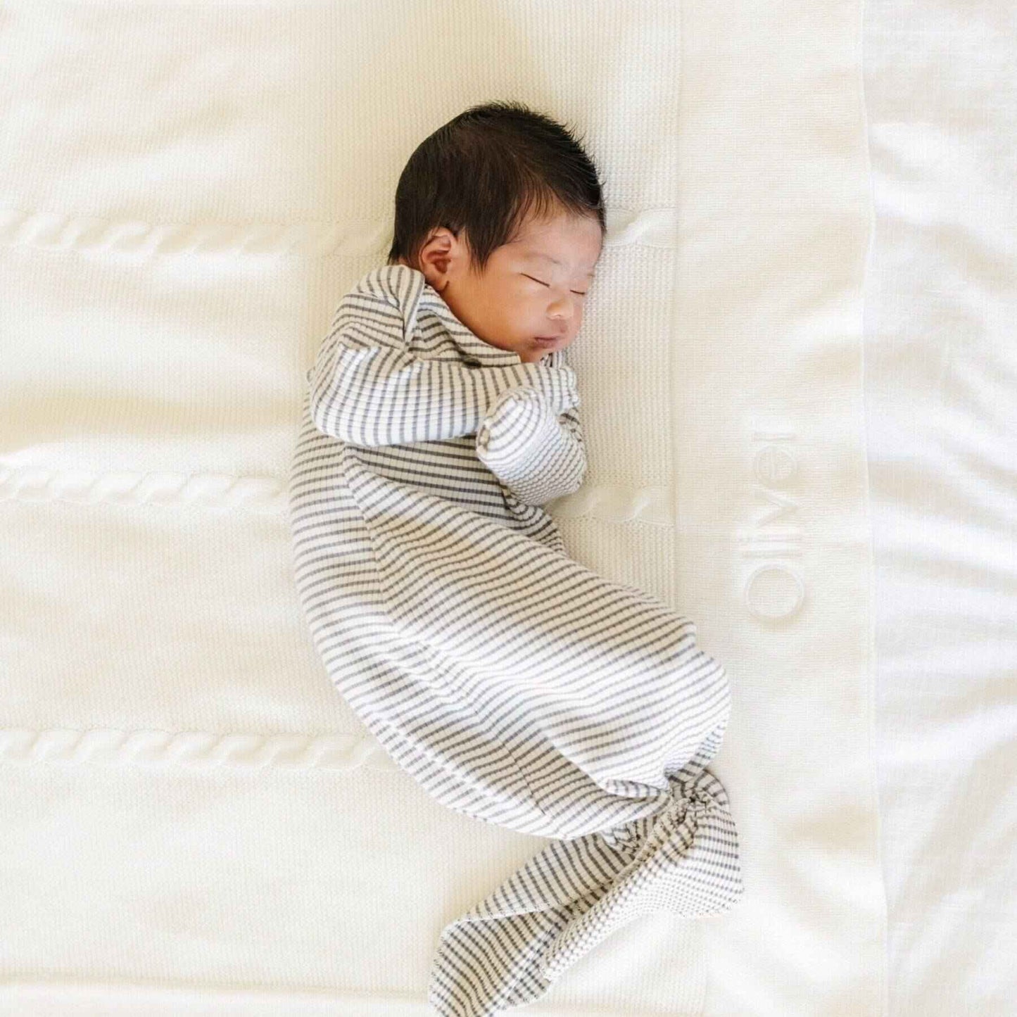 Newborn baby swaddled in a striped blanket on Saranoni Heirloom Cotton Knit Receiving Blanket Cream