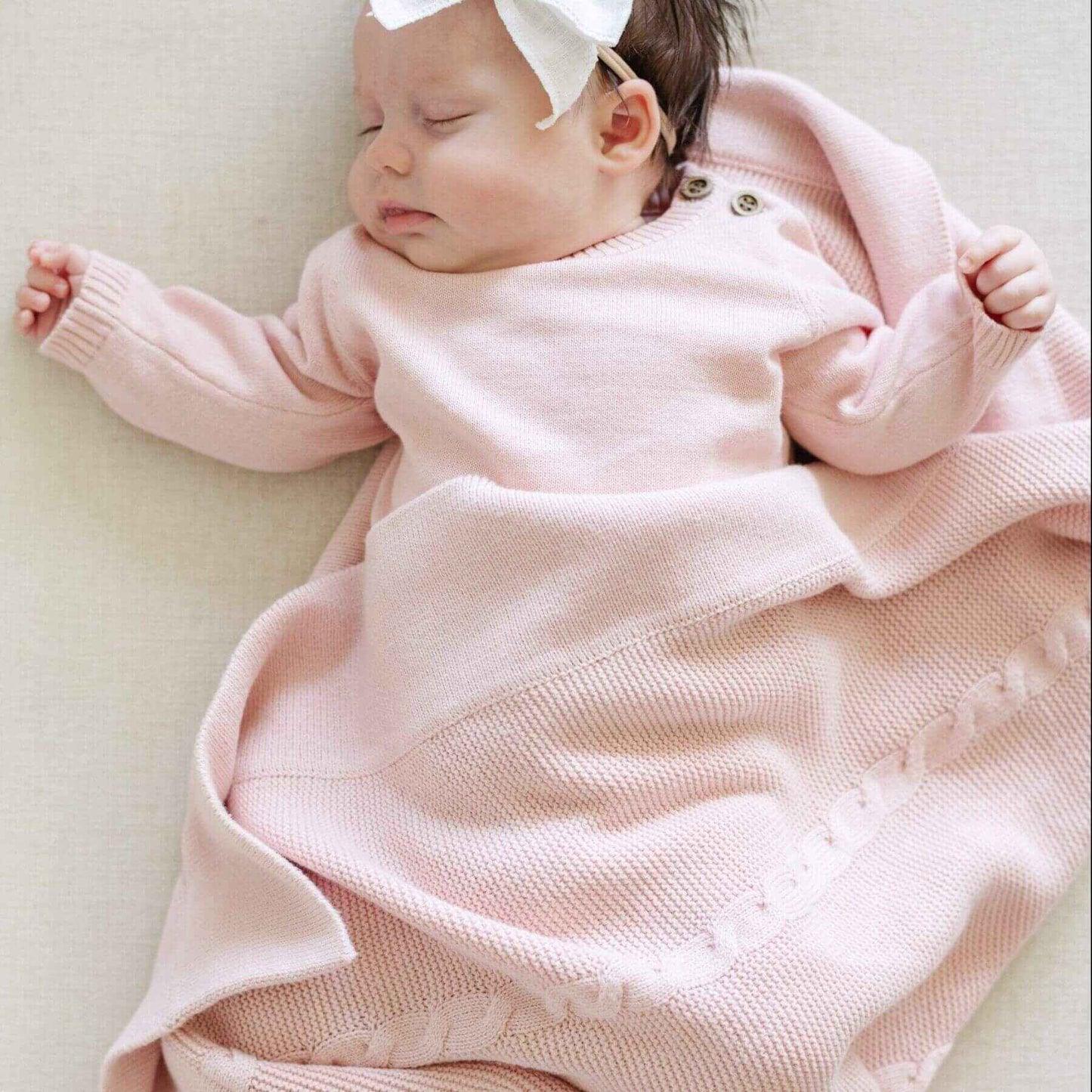 Baby wrapped in Saranoni Heirloom Cotton Knit Receiving Blanket with a white bow on a light background