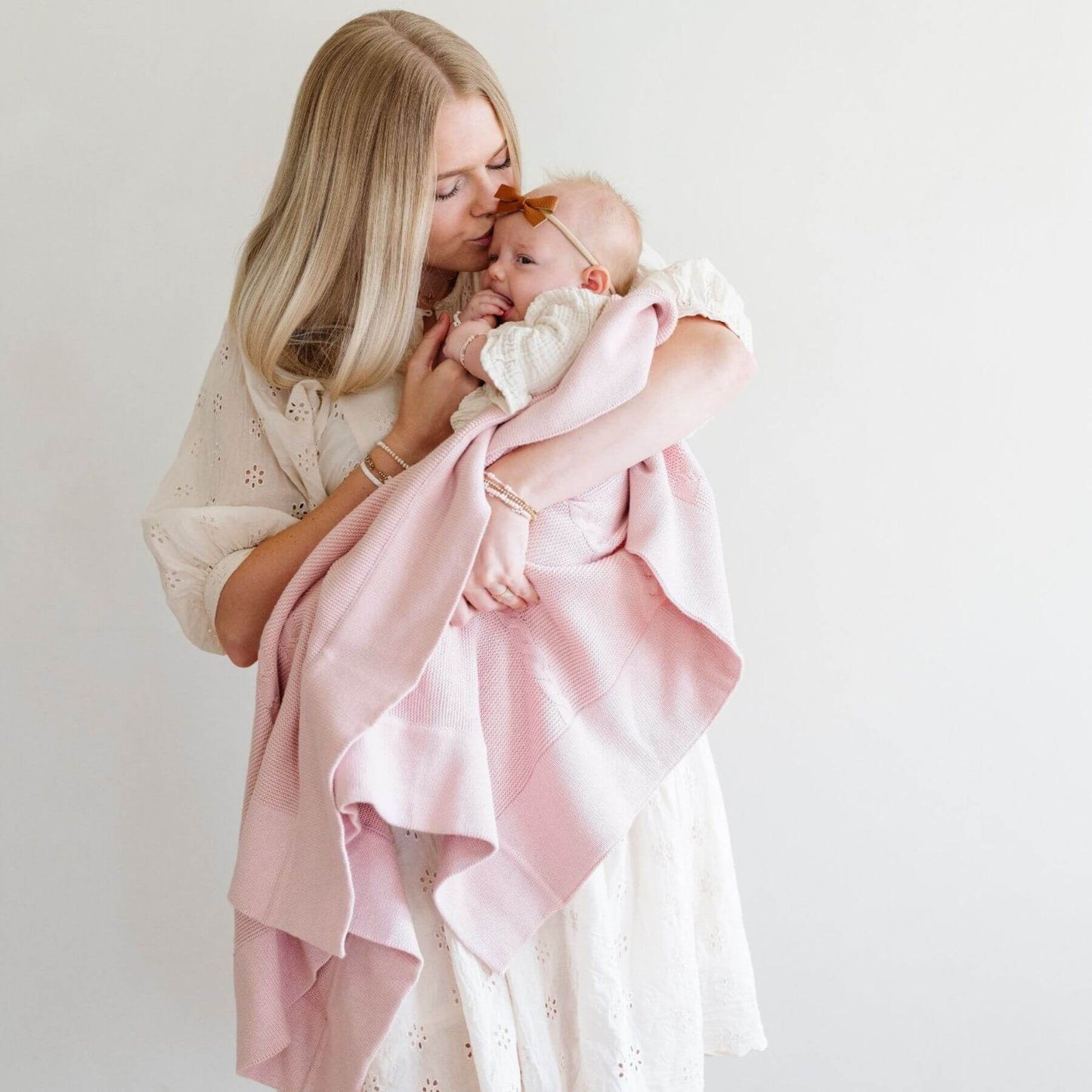 Woman holding a baby wrapped in Saranoni Heirloom Cotton Knit Receiving Blanket against a white background