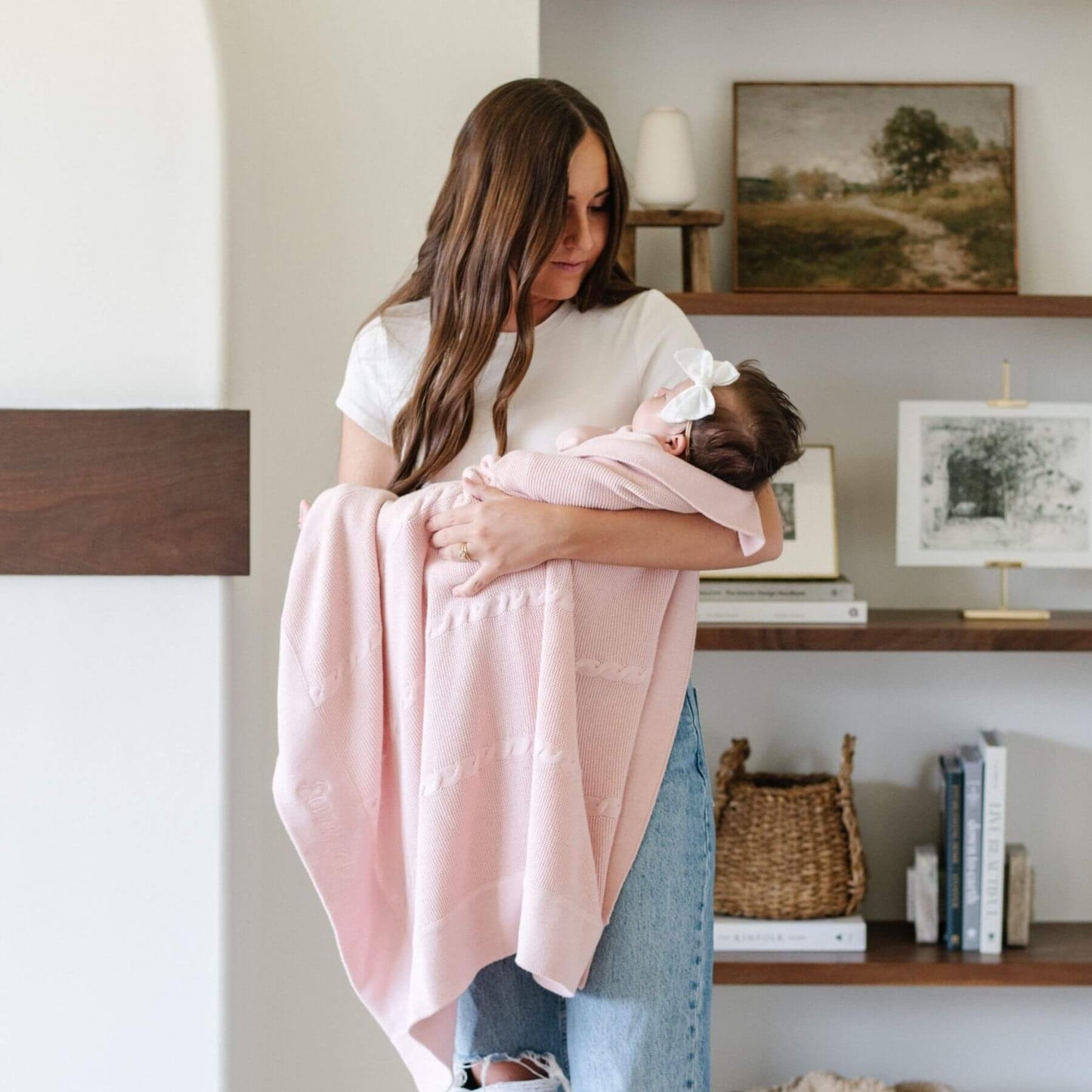 Woman holding a baby wrapped in Saranoni Heirloom Cotton Knit Receiving Blanket in a home setting